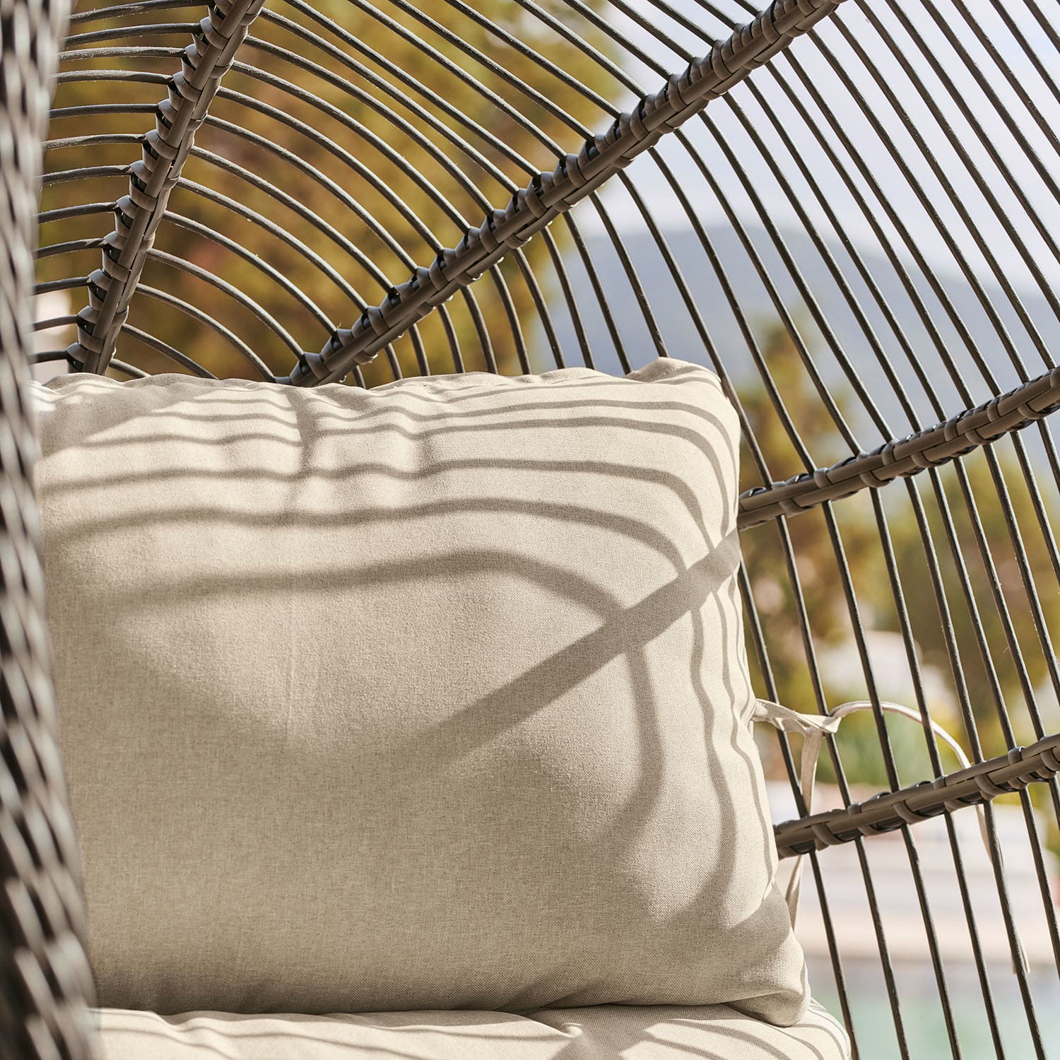 Beiges Stoffkissen auf braunem Rattansessel im sonnigen Außenbereich