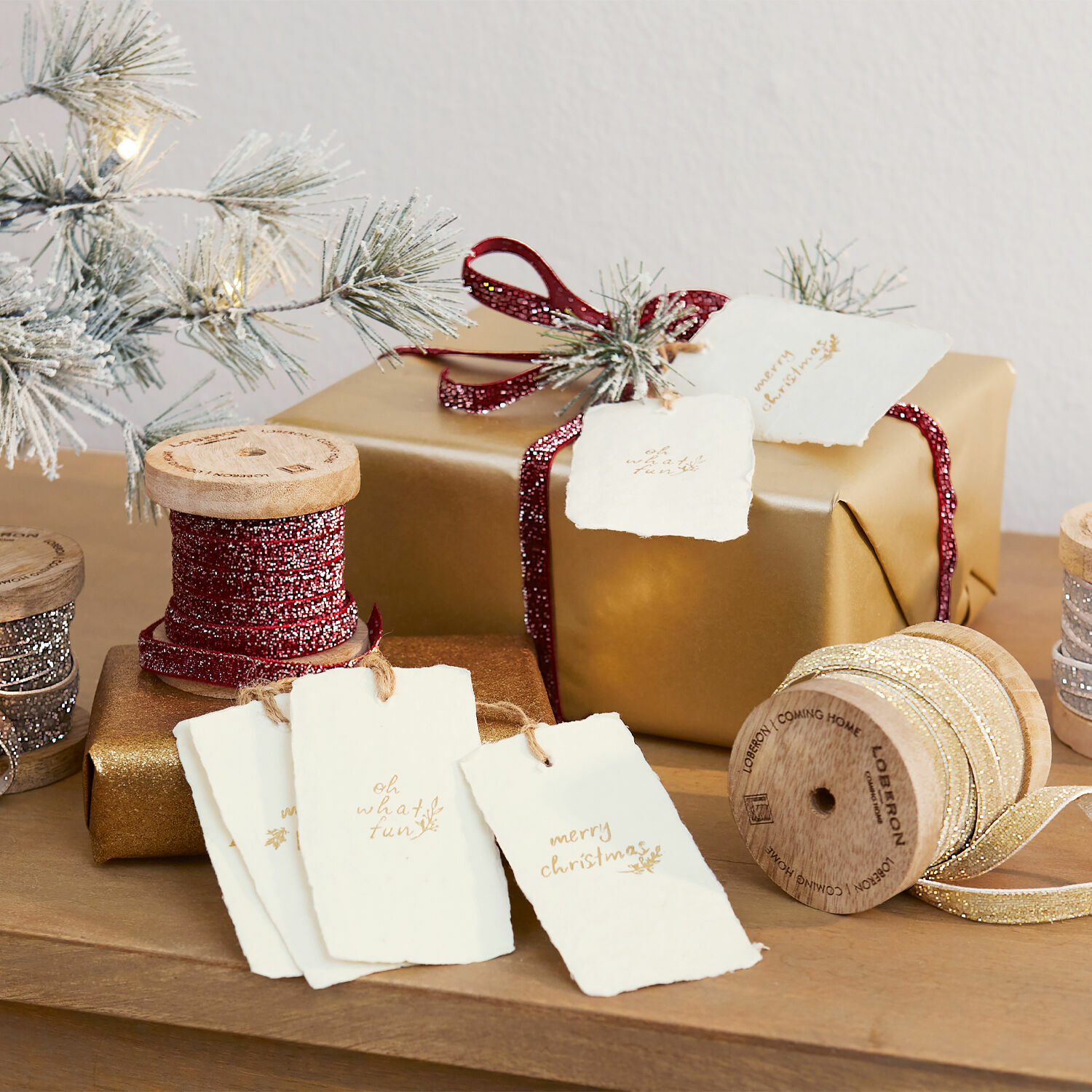 Goldene und rote Bänder auf Holzspulen mit Papier-Weihnachtsetiketten auf Holztisch arrangiert