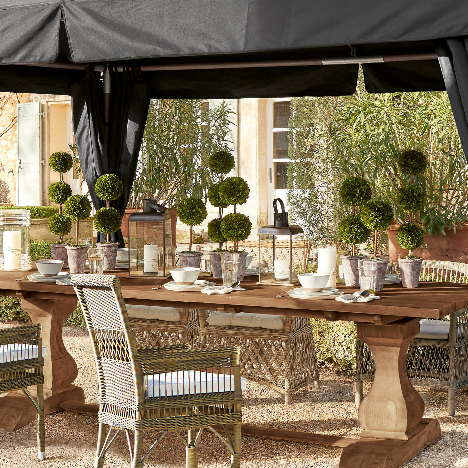 Großer Holzgarten-Tisch mit Rattanstühlen und grünen Topfpflanzen auf der Terrasse