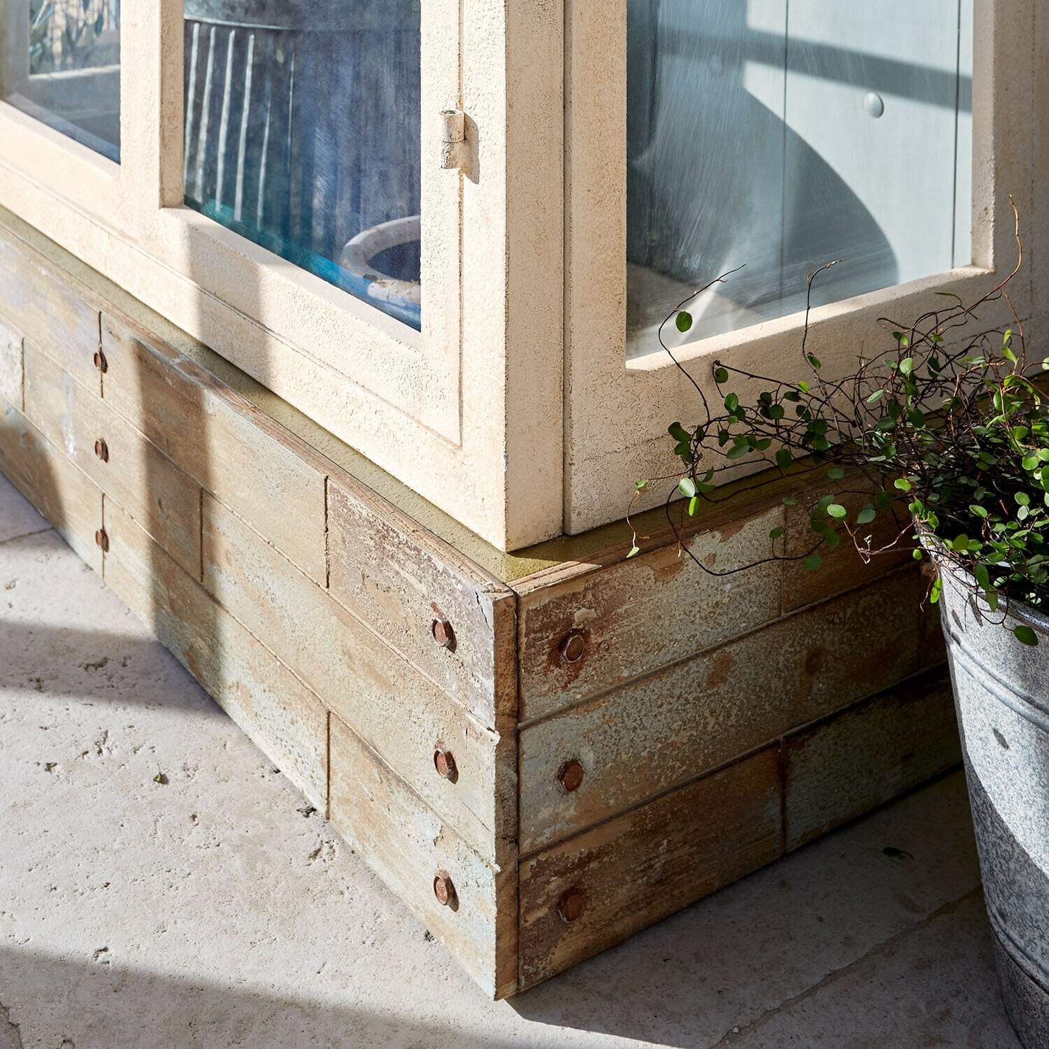 Ecke aus hellem Holz mit Metallnieten und grünem Topfpflanze im Außenbereich bei Sonnenlicht