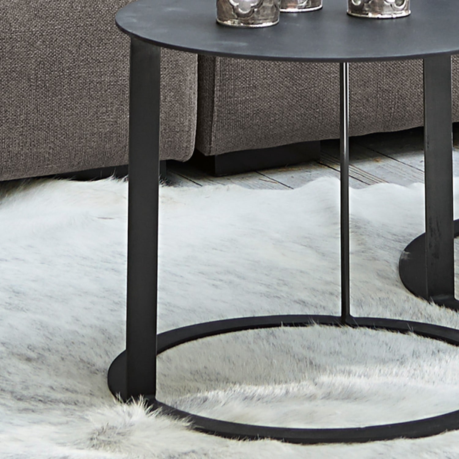 Schwarzer Metall-Couchtisch mit runder Basis auf hellem Fellteppich im Wohnzimmer