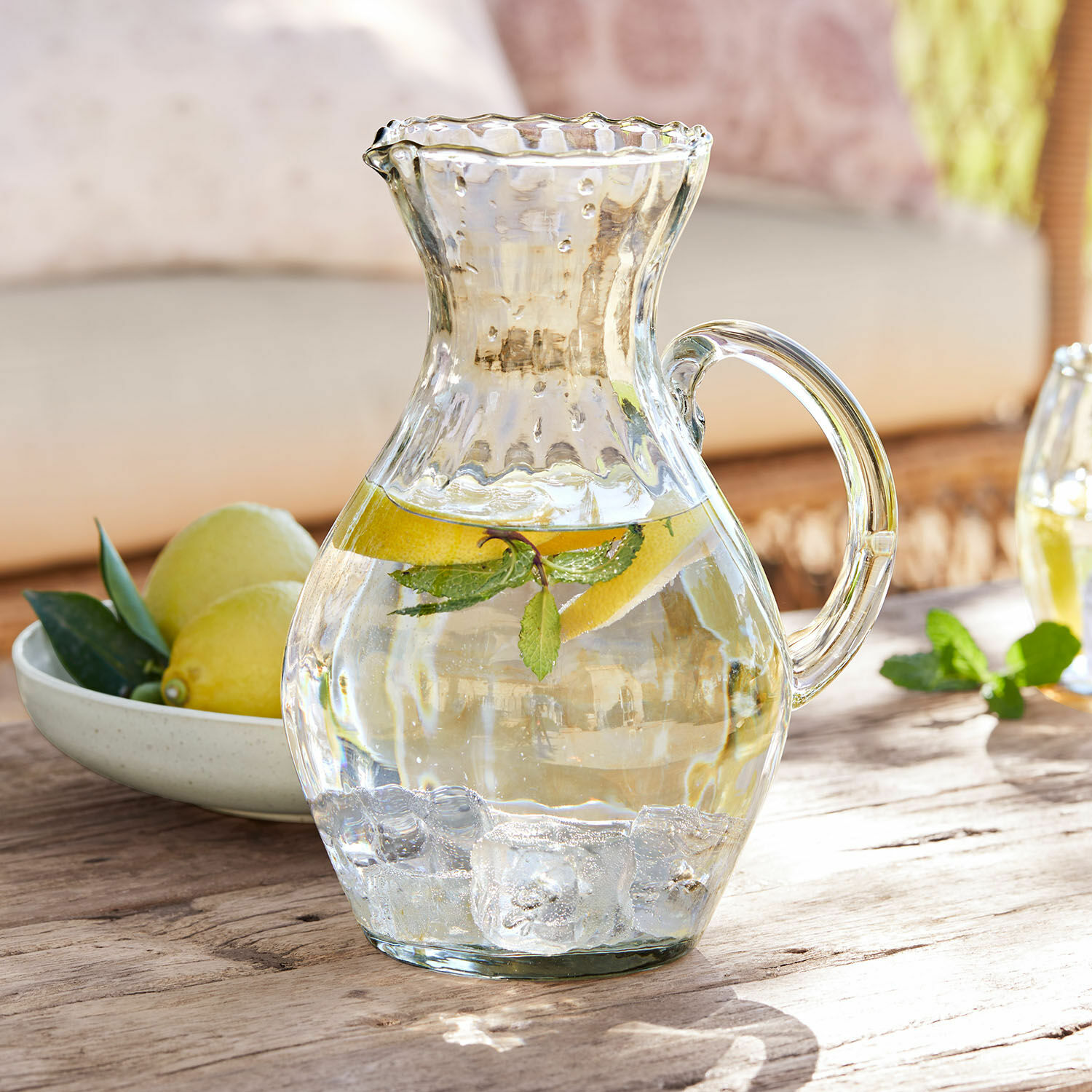 Karaffe Bourgavin Glaskrug mit Wasser, Eiswürfeln, Zitrone und Minze auf Holztisch, erfrischendes Sommergetränk