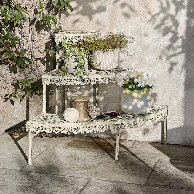 Cremefarbene Metall-Etagere mit filigranem Muster, dekoriert mit Blumentöpfen, Gartendeko