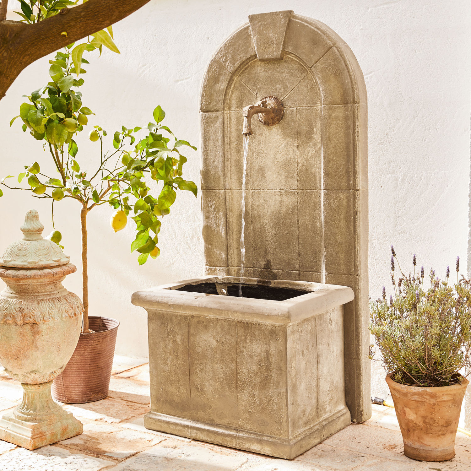 Dekorativer Gartenbrunnen aus beigem Stein mit Metallhahn und fließendem Wasserstrahl