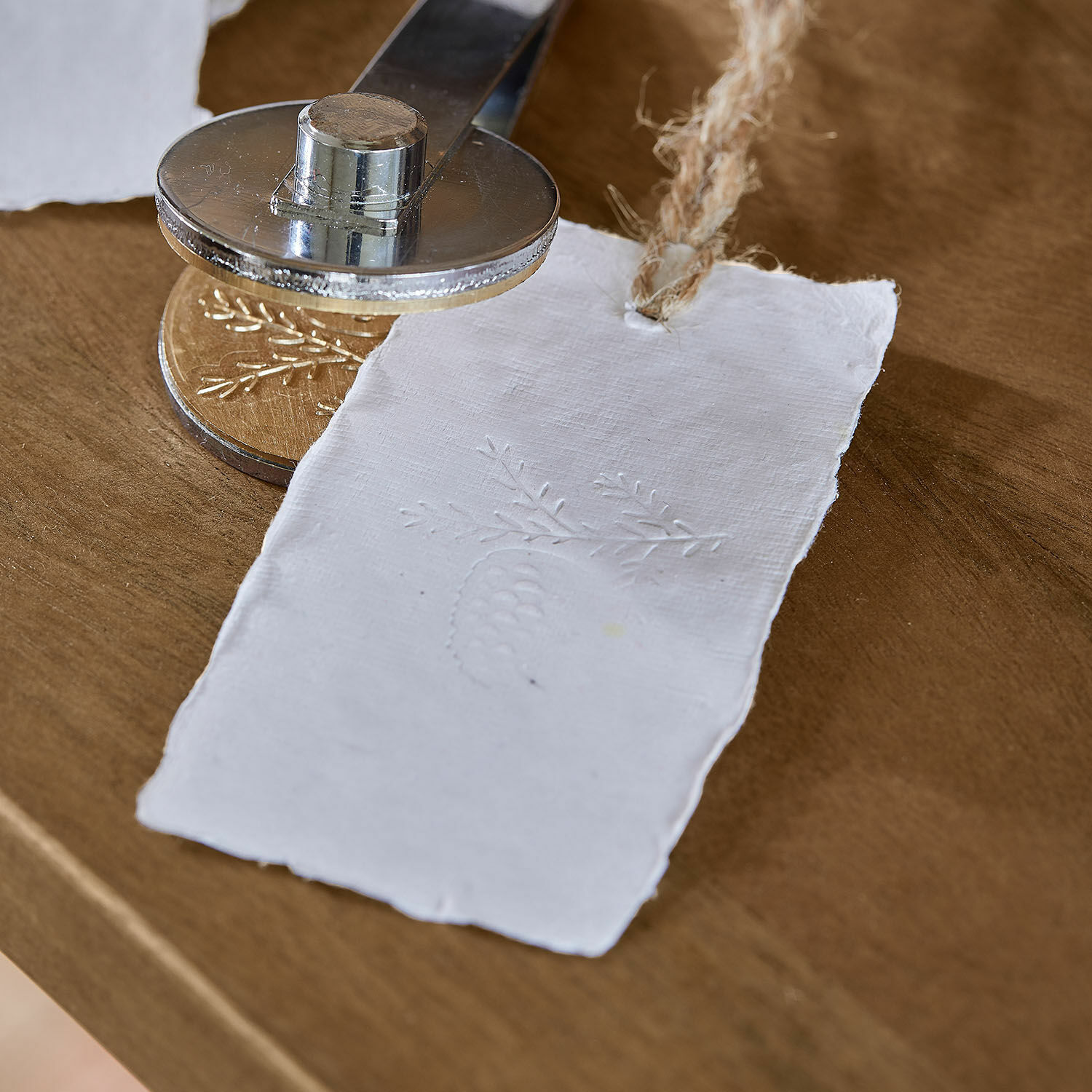 Metallprägestempel prägt Muster auf weißem Papier mit Kordel auf Holztisch