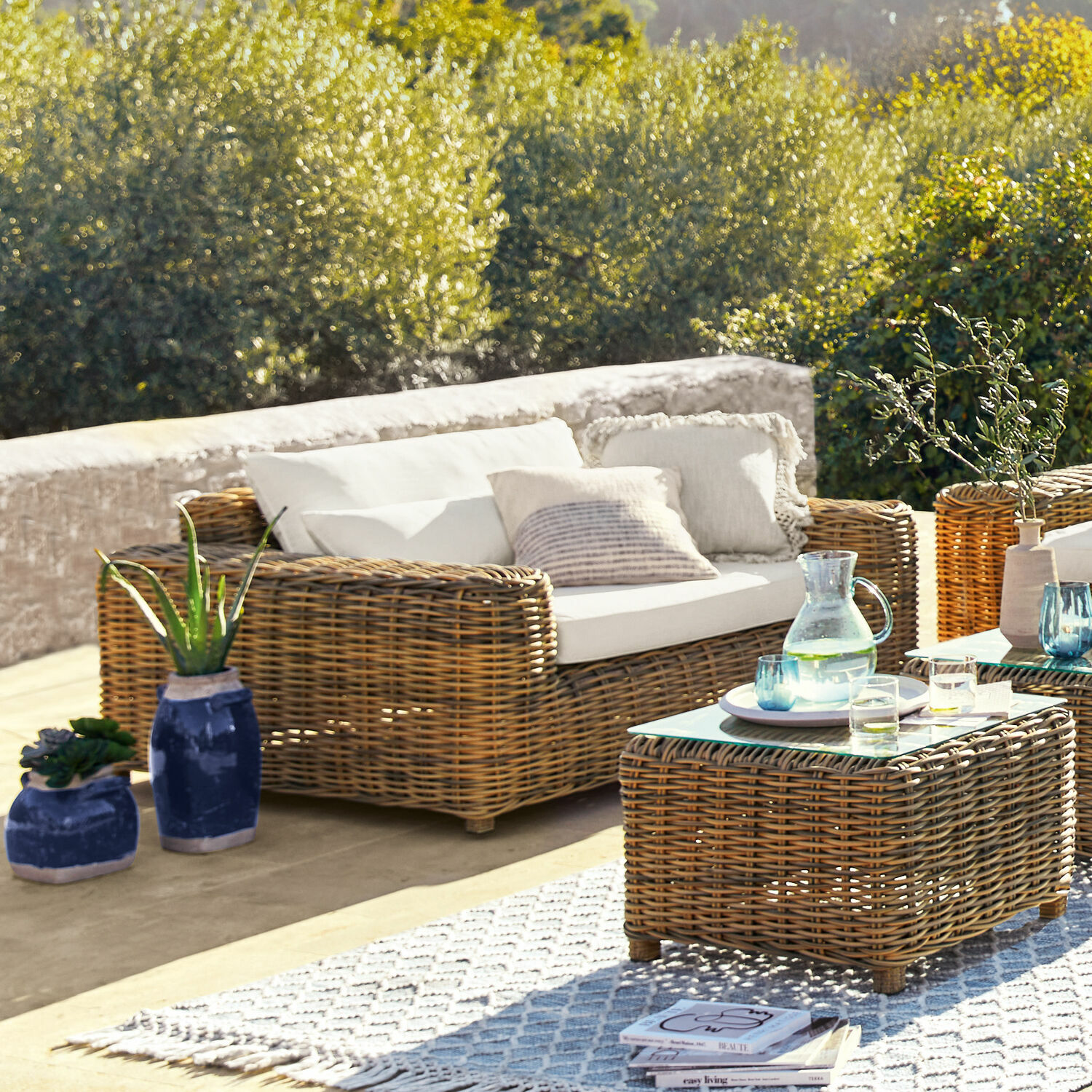 Gartenmöbel-Set aus natürlichem Rattan mit weißen Kissen und Glastisch auf Terrasse