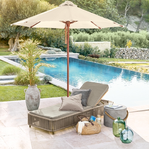 Gartenliege mit beigem Polster und Sonnenschirm am Pool, Dekoration aus Rattan und Glas