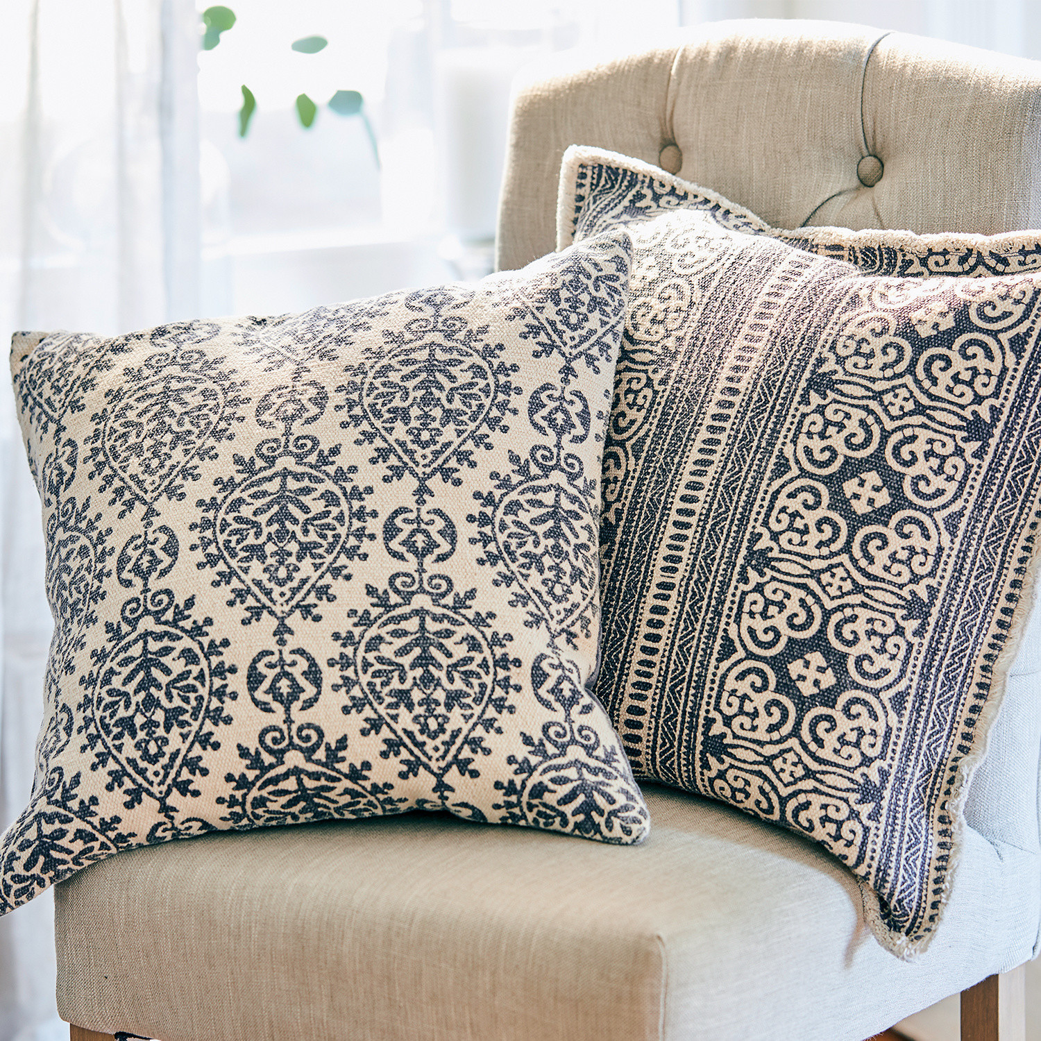 Zwei dekorative Baumwollkissen in Beige mit blauen Mustern auf hellem Sessel im Wohnzimmer