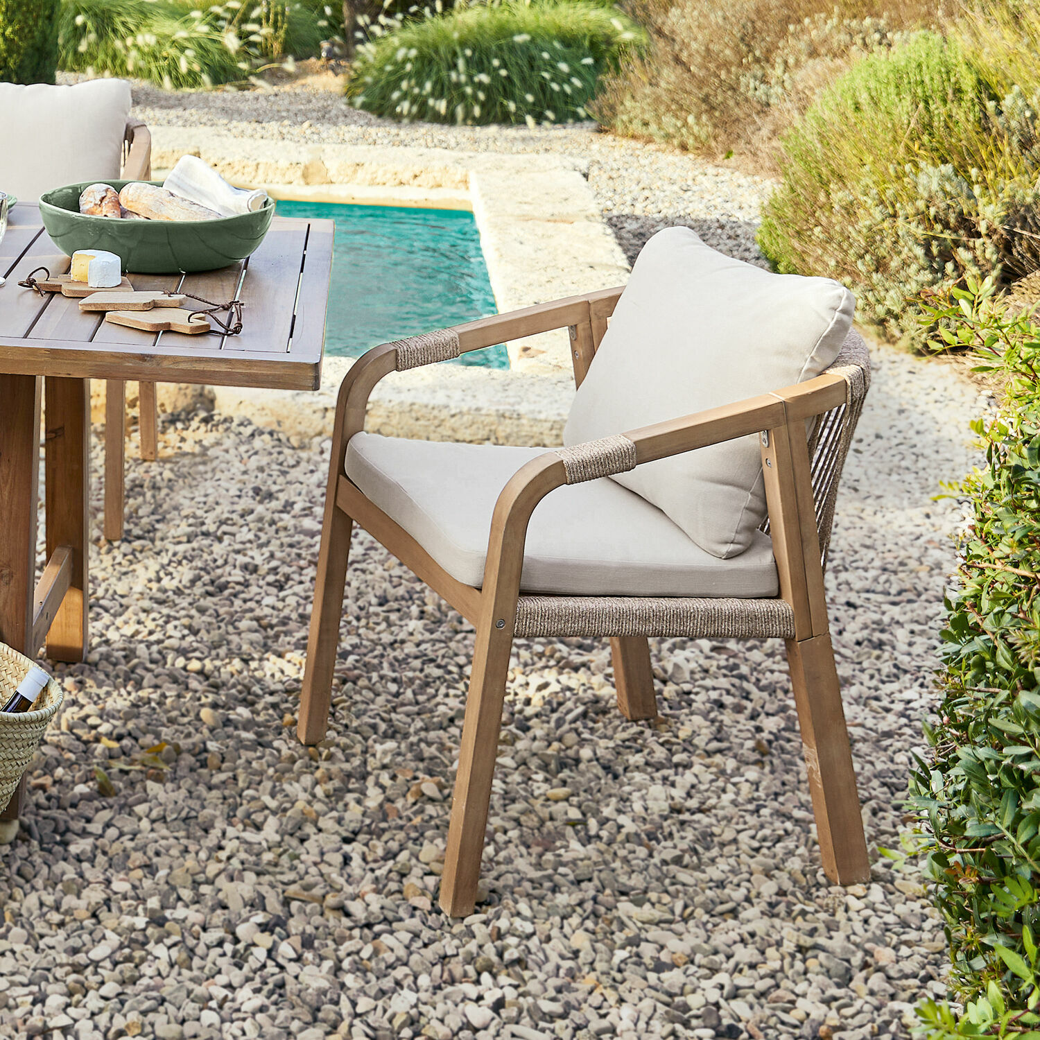 Gartenstuhl aus Holz mit hellen Polstern auf Kieselstein-Terrasse neben Pool