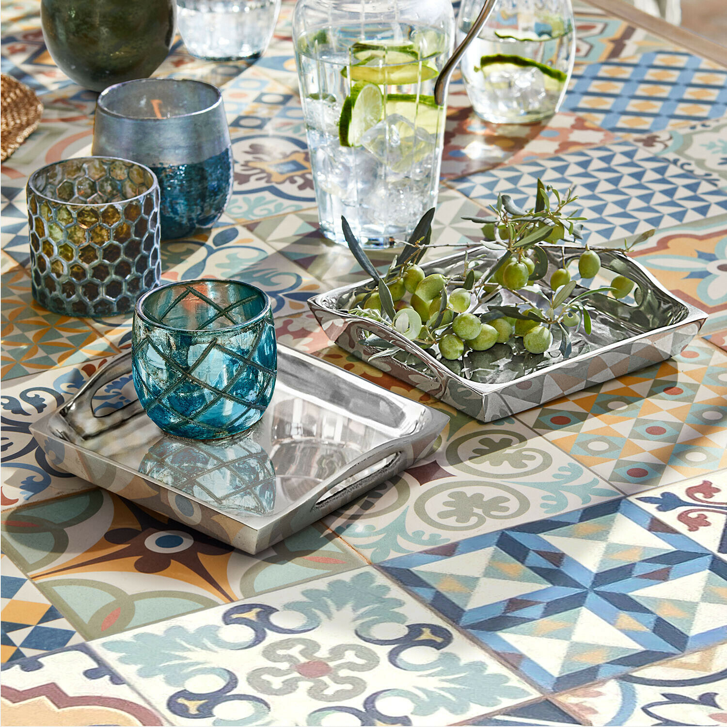 Beidseitige silberne Metalltabletts auf buntem Mosaiktisch mit blauen Glaswindlichtern und grünen Oliven