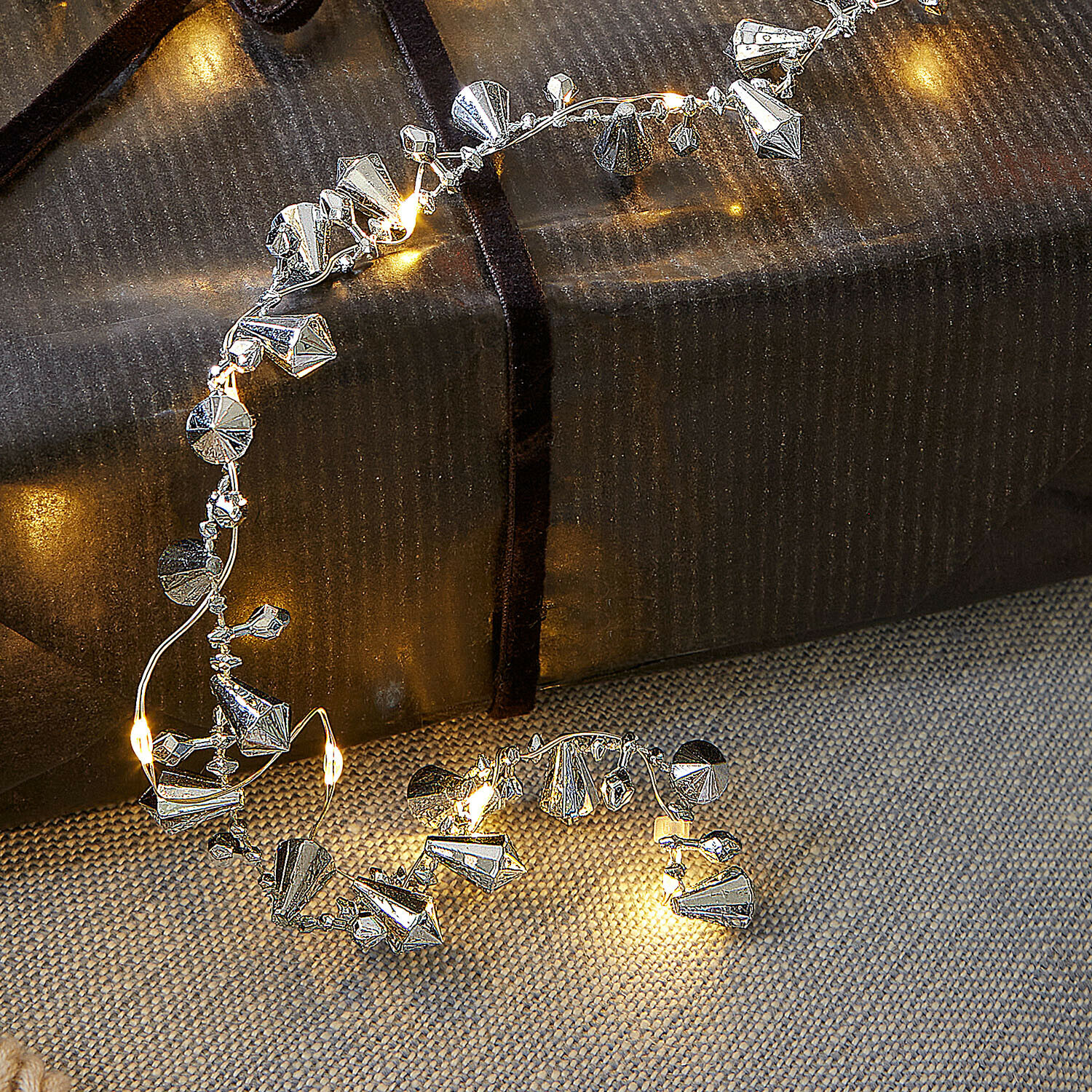 Feine silberne Dekokette mit kleinen LED-Lichtern auf Geschenk und Stoffuntergrund