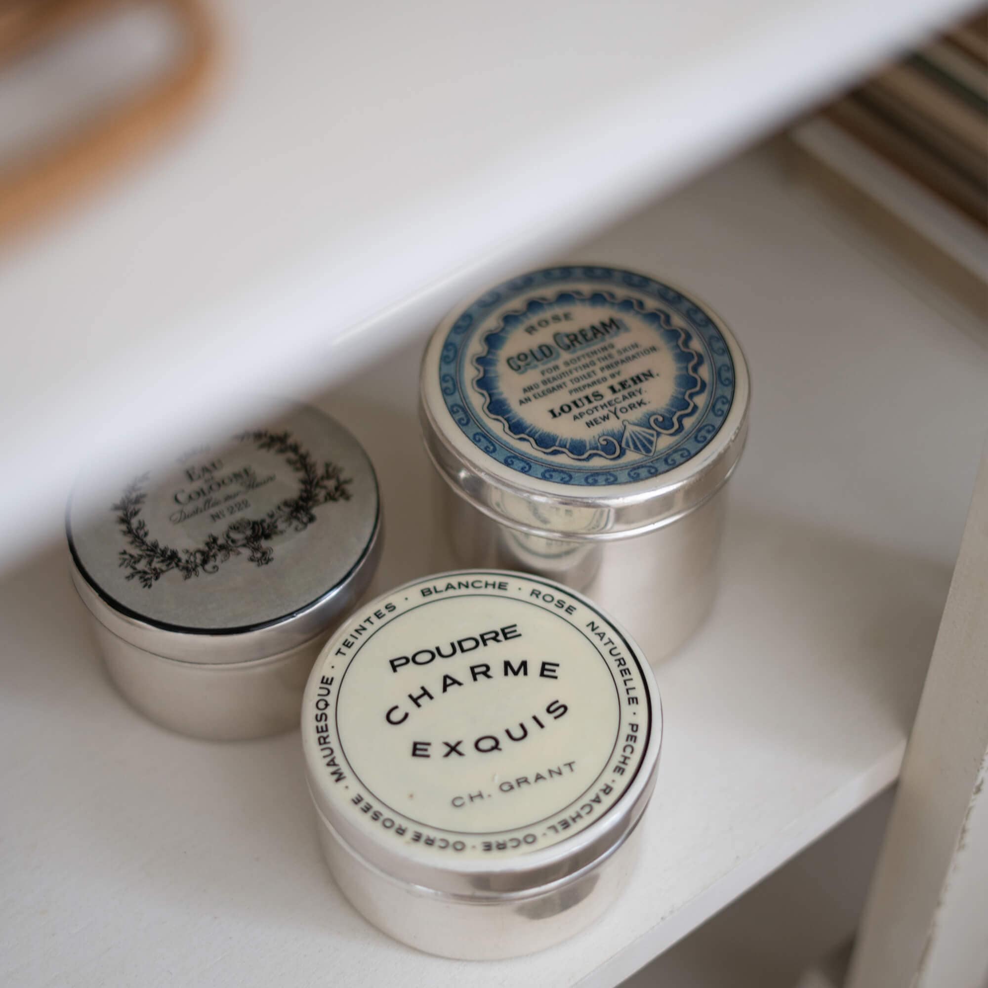Drei metallene Vintage-Dosen mit Kosmetikaufklebern auf weißem Regal zur Aufbewahrung