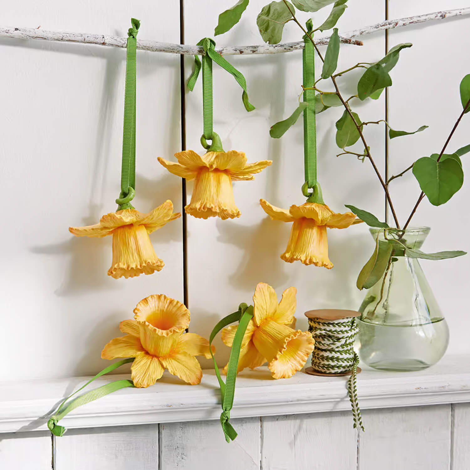 Gelbe Blumen-Dekorationen mit grünen Bändern an weißem Regal, Frühlingsdeko für Zuhause
