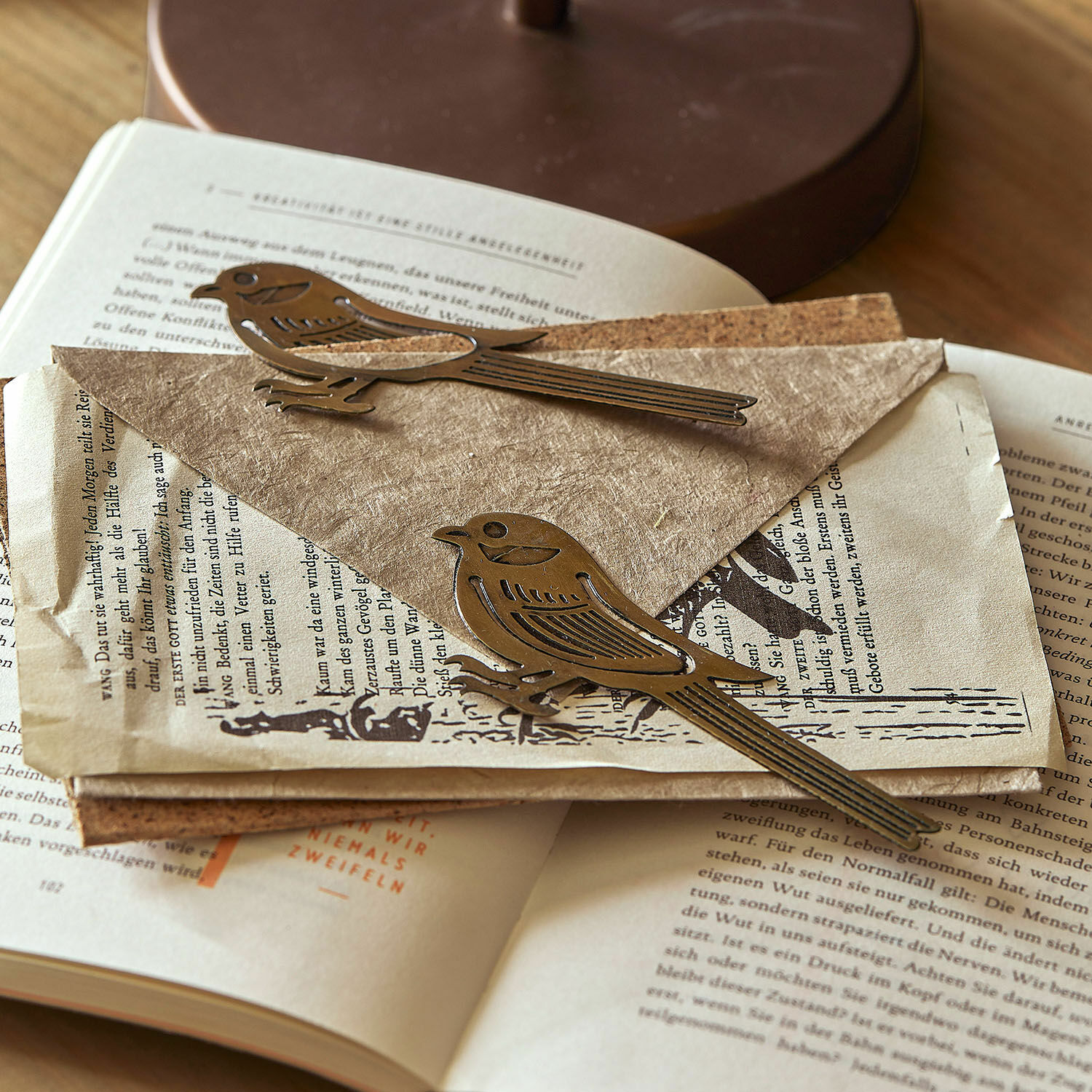 Metallische Briefklammern in Vogel-Form aus Messing auf alten Papieren und einem aufgeschlagenen Buch