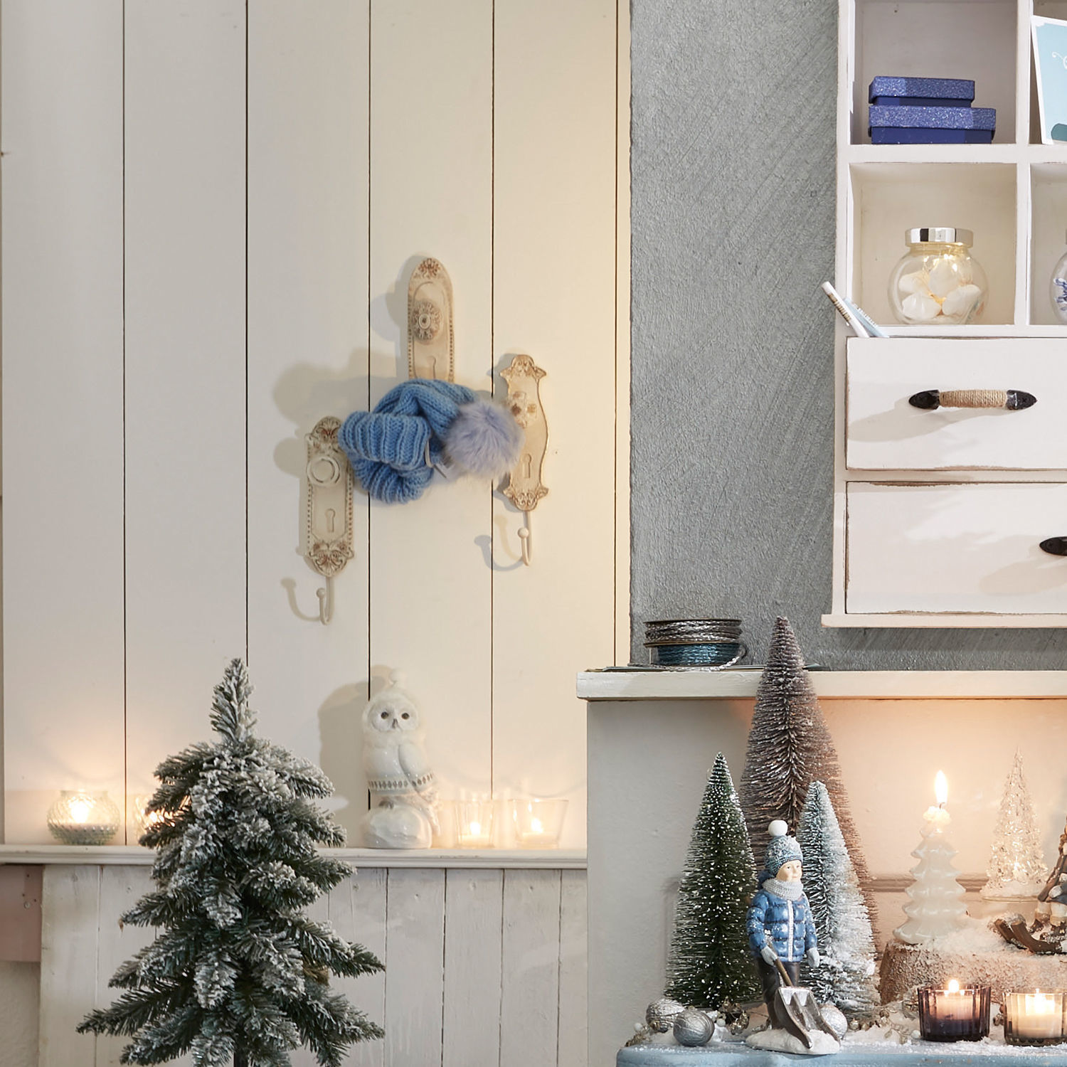 Winterliche Dekoration mit kleinen Tannen, Kerzen und Kinderfigur in blauer Jacke für Weihnachten