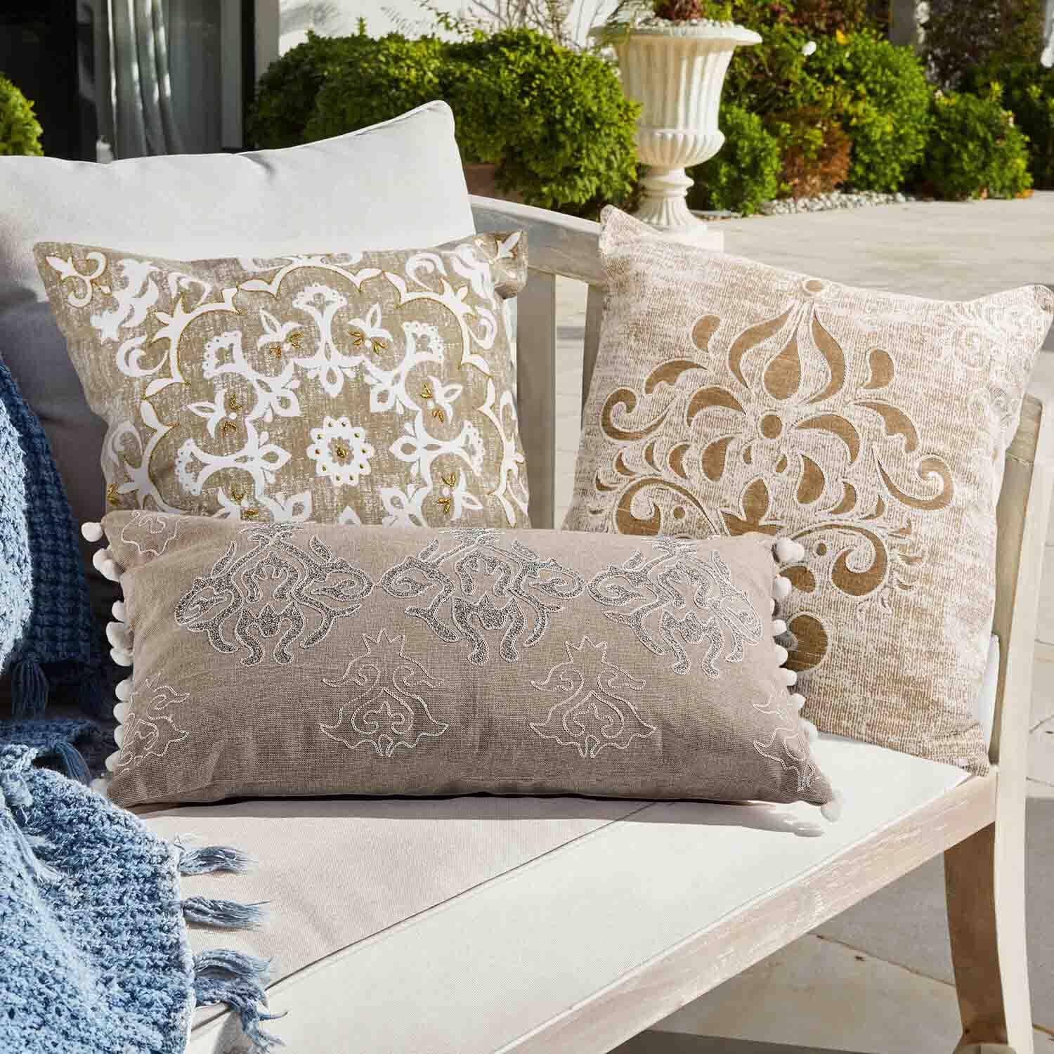 Drei dekorative Kissen in Beige und Weiß mit Mustern auf hellem Sofa im Garten