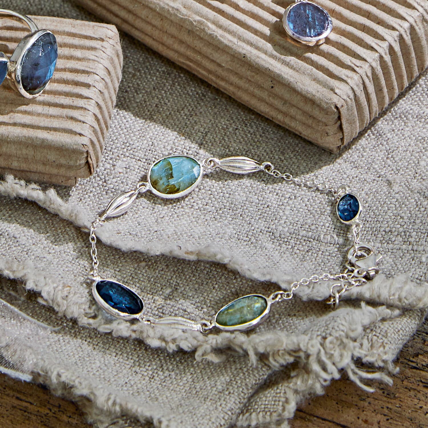 Silberarmband mit blauen und grünen Steinen auf Leinenstoff, eleganter Damenschmuck