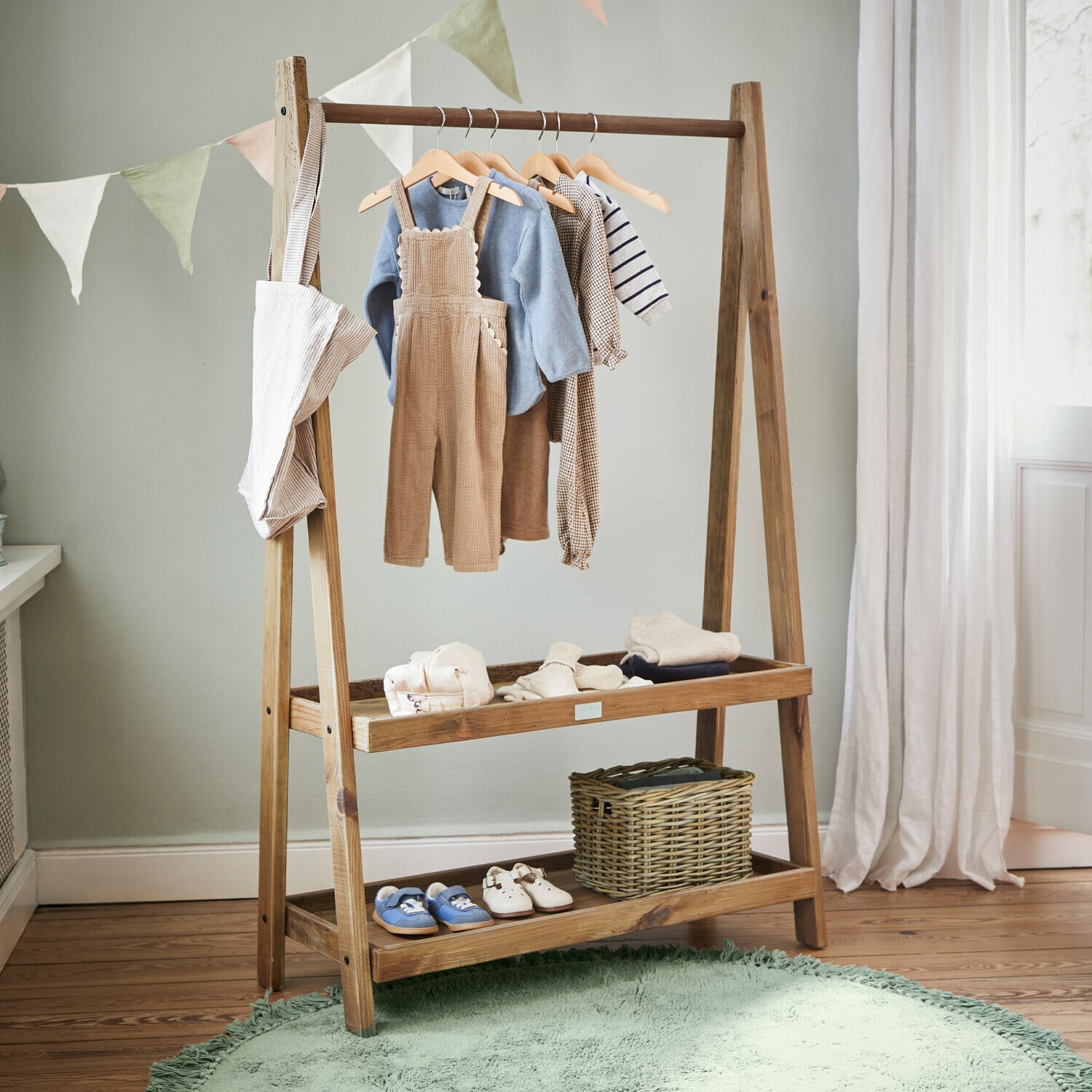 Holz-Kleiderständer mit Kinderkleidung und Schuhen in hellem Raum mit grünem Teppich