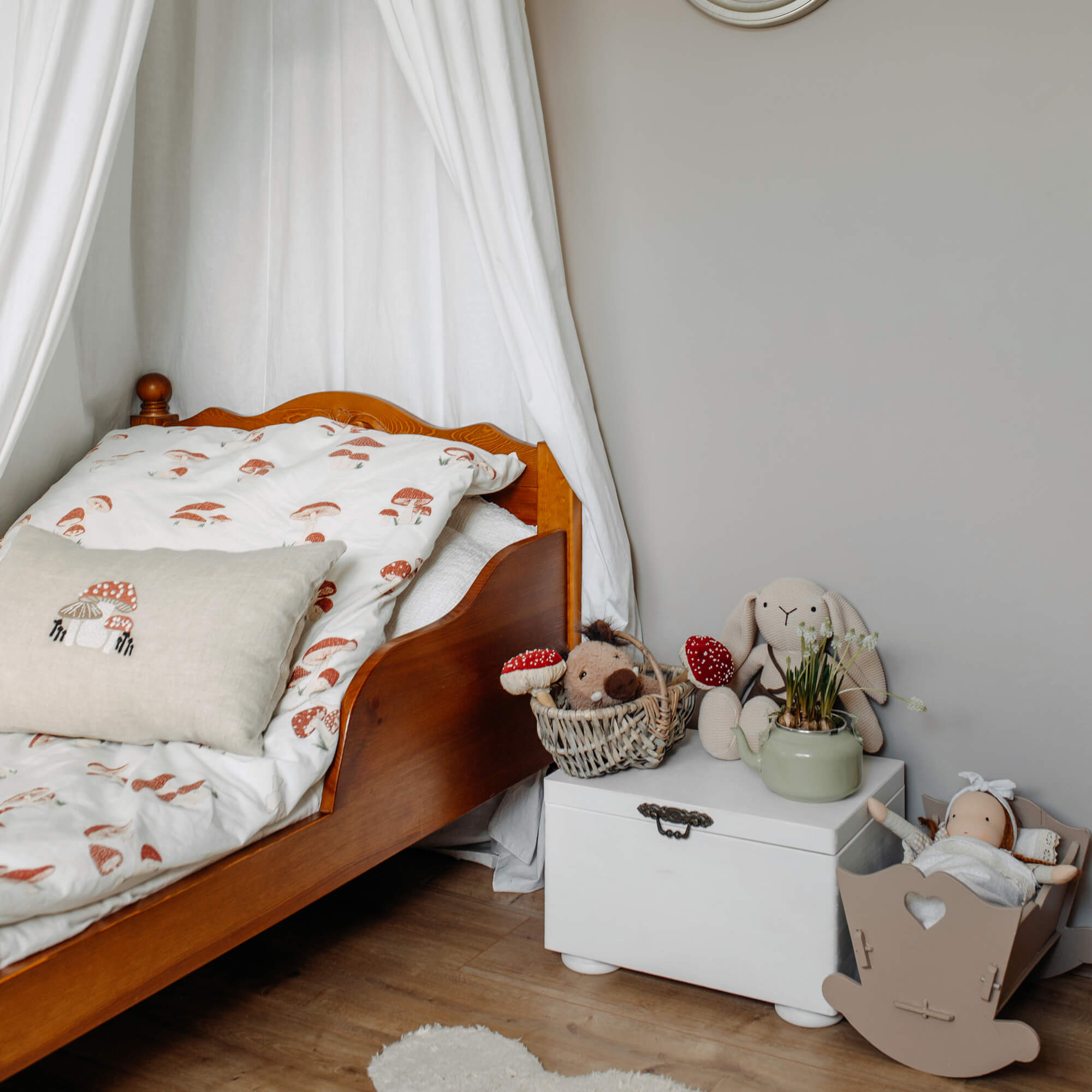 Kinderbett aus Holz mit weißer Bettwäsche mit Pilzmotiv und Kuscheltieren auf weißer Truhe