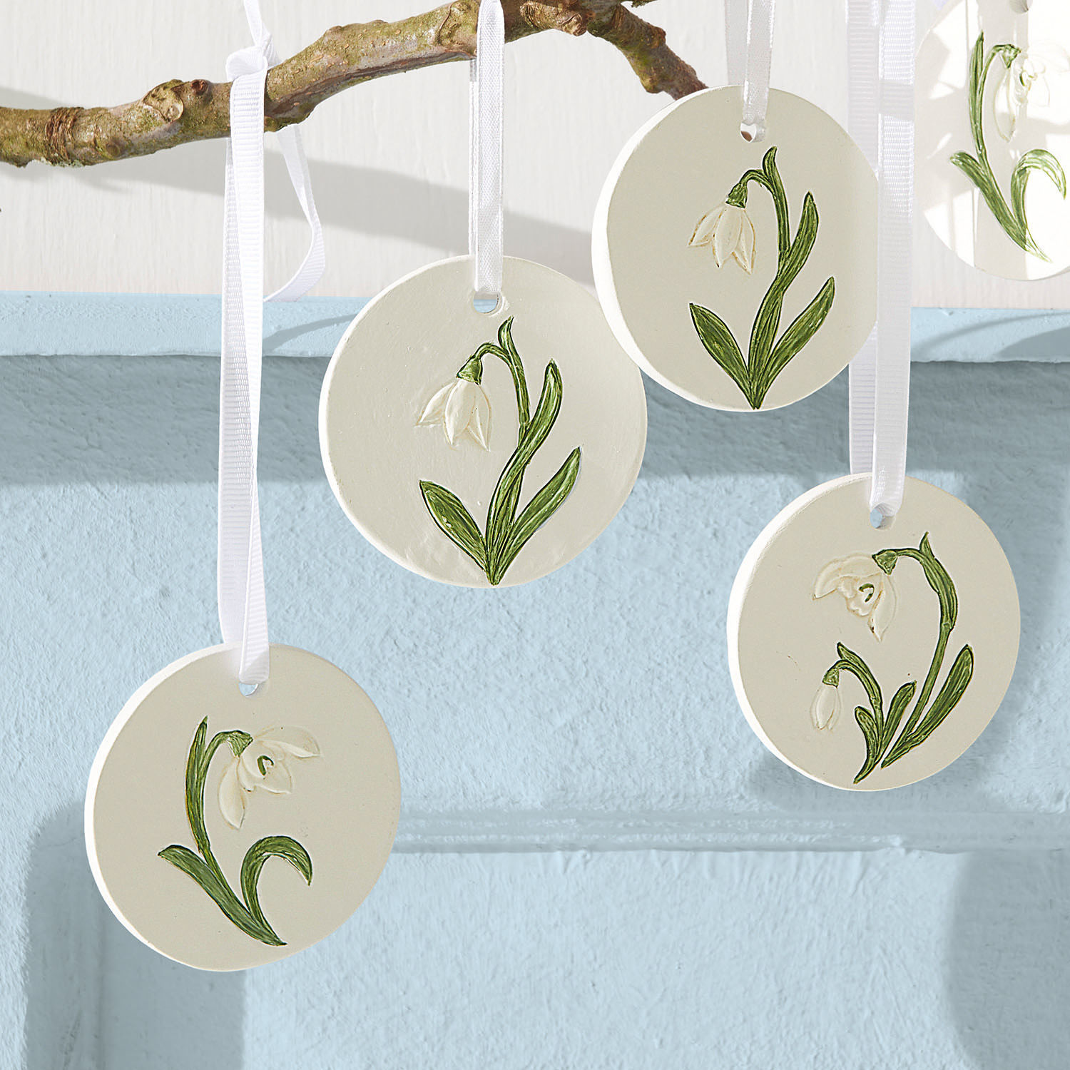 Runde weiße Tonanhänger mit grünen Blumenmotiven an weißen Bändern als Dekoration