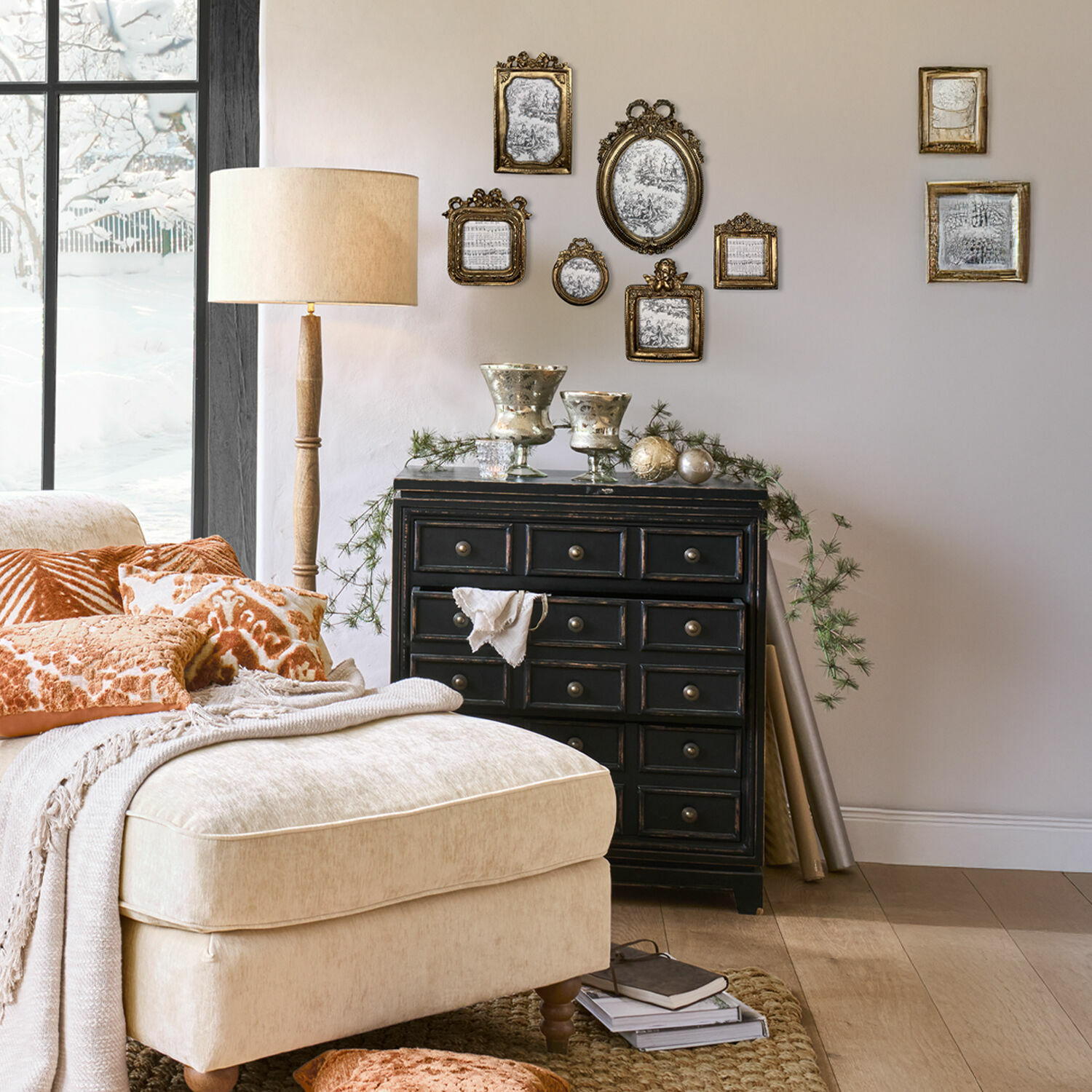 Bequemer beiger Sessel mit orangen Kissen und schwarzer Kommode mit goldenen Bilderrahmen an der Wand