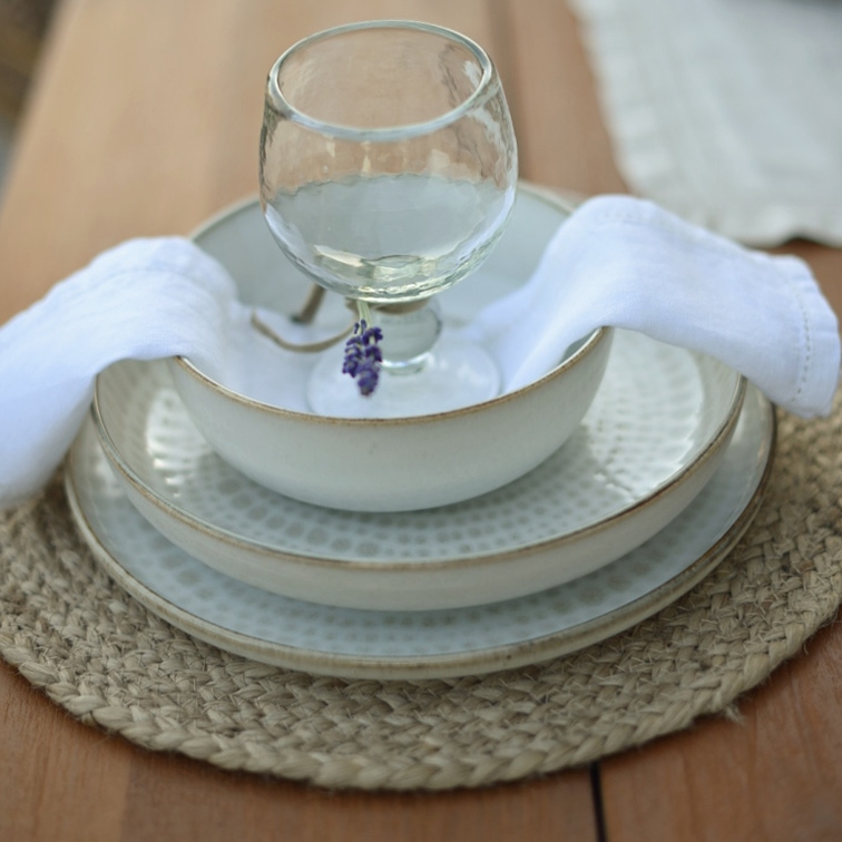 Set aus weißer Keramik mit Tellern und Schale auf geflochtenem Platzset mit weißer Serviette