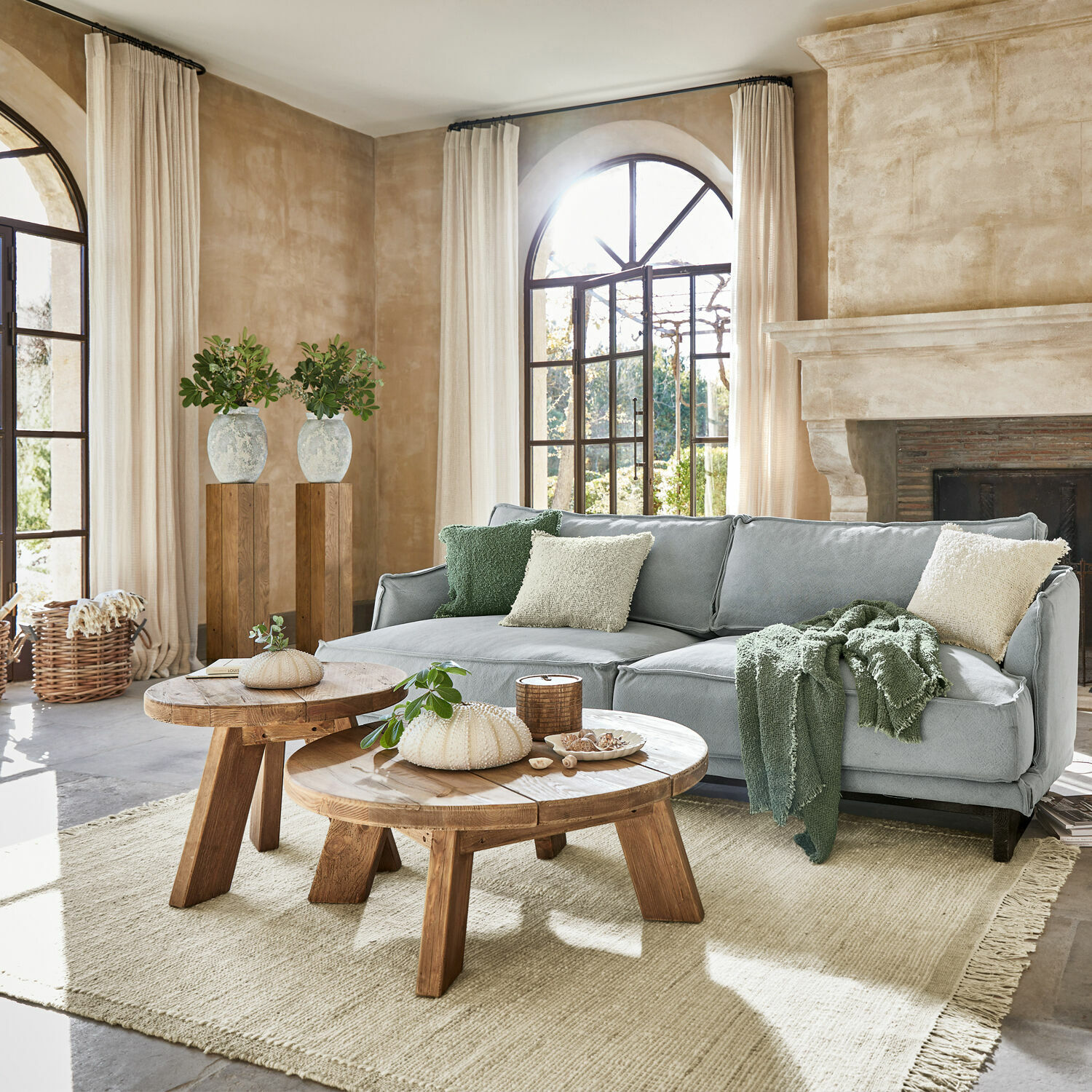 Teppich Placidia Gemütliches Wohnzimmer mit grauem Sofa, runden Holztischen und hellem Naturteppich im Landhausstil