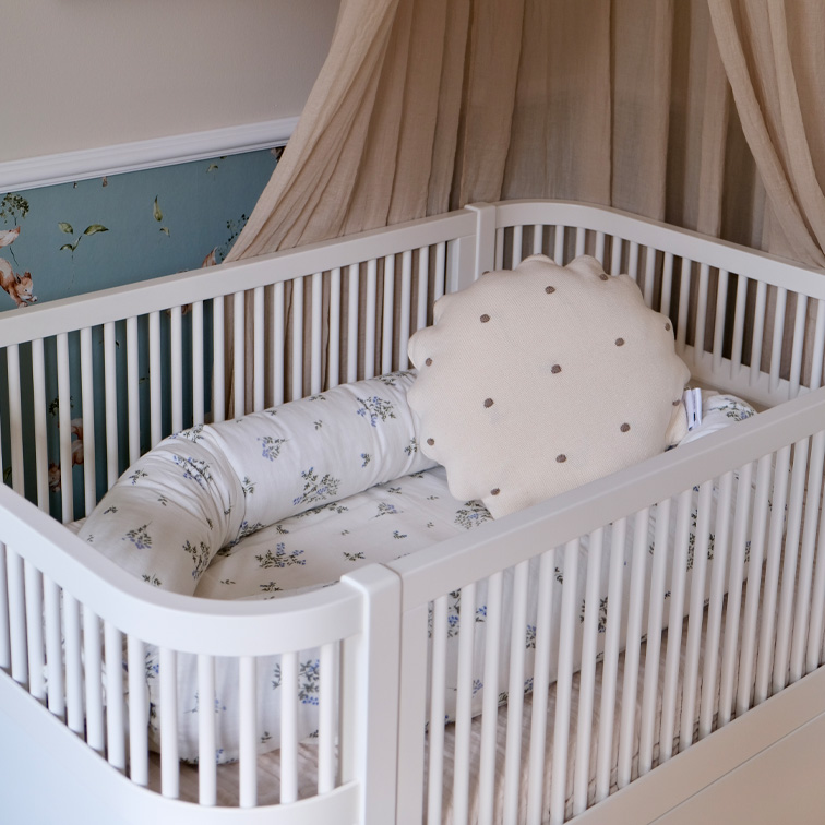 Weißes Babybett mit weichem Kissen und floralem Bettzeug in Pastellfarben