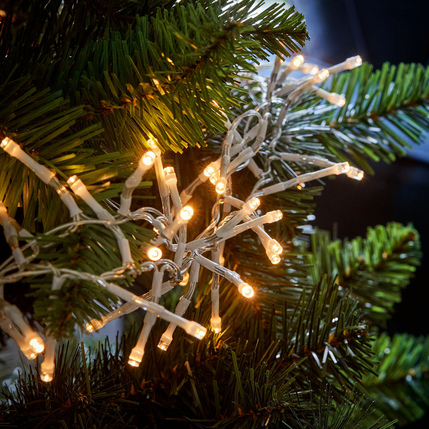 LED-Lichterkette mit weißem Kabel an grünen Zweigen eines künstlichen Weihnachtsbaums, Weihnachtsdeko