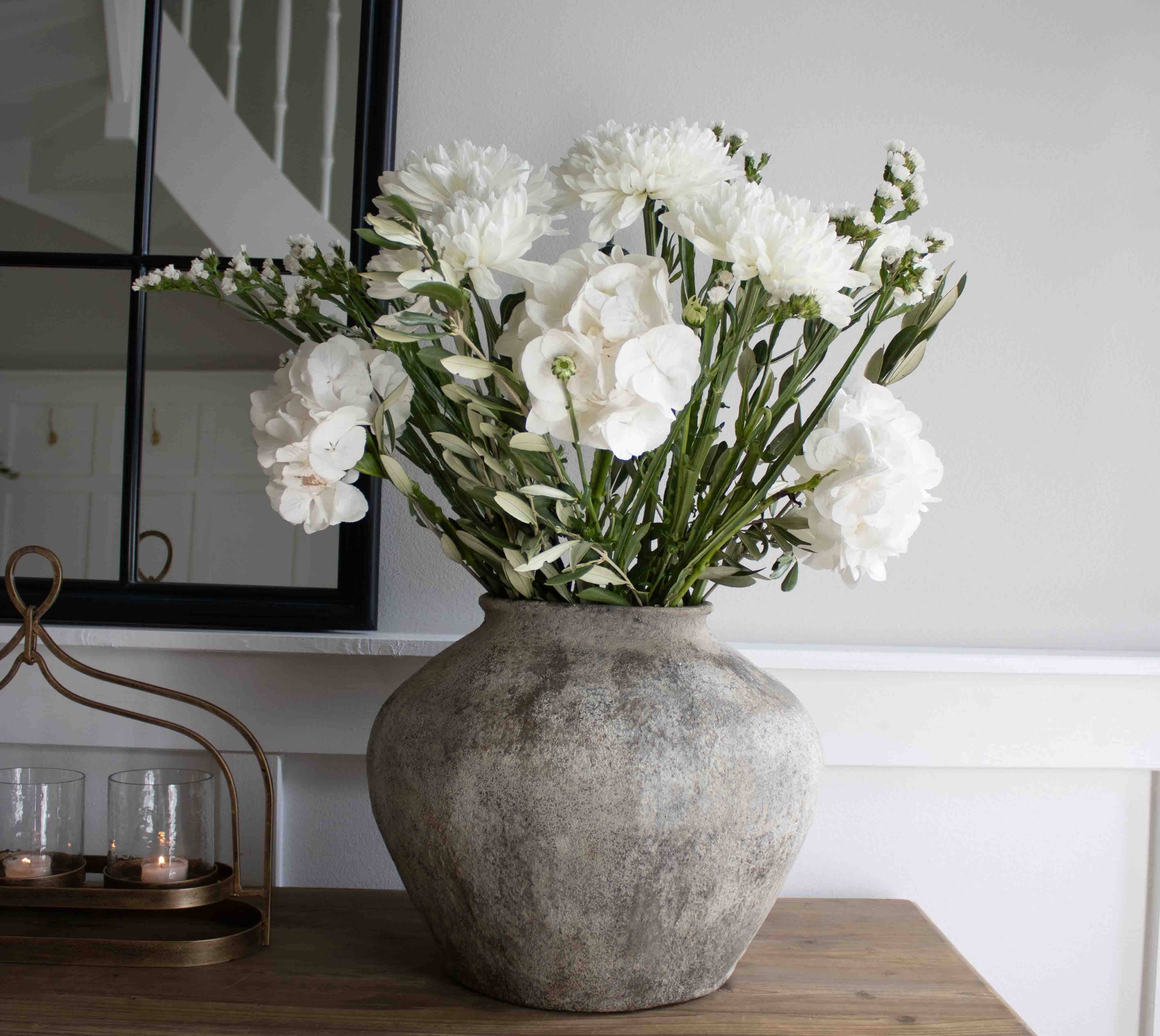 Große graue Steinvase mit weißen Dekoblumen auf Holztisch im Wohnzimmer