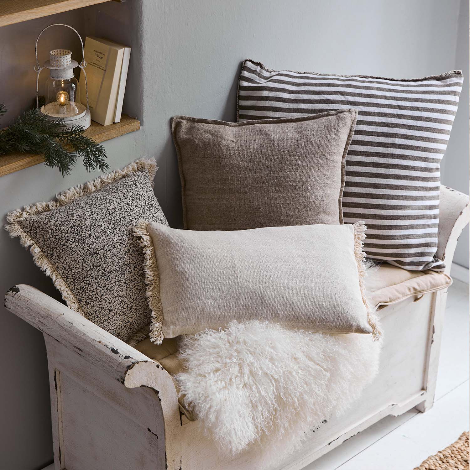 Set dekorative Kissen in Beige- und Brauntönen auf weißer Holzbank mit flauschiger Decke