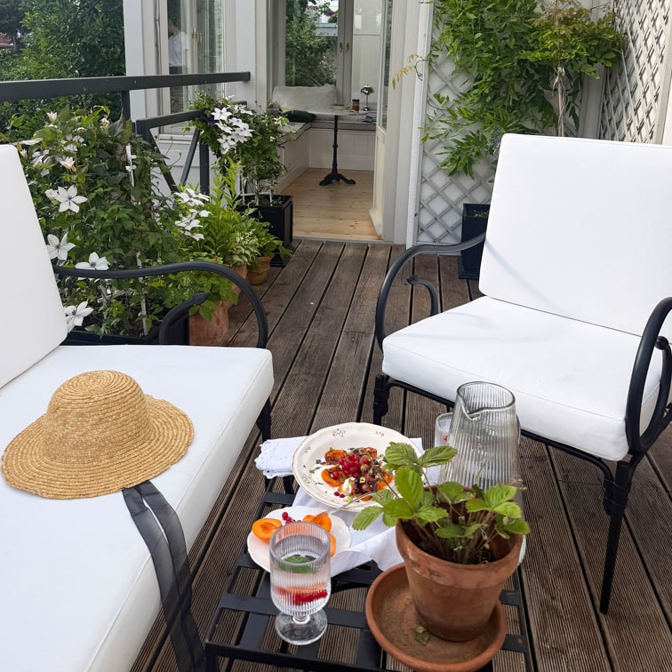 Terrasse mit weißen Metallstühlen, Holzboden und Topfpflanzen für gemütlichen Außenbereich