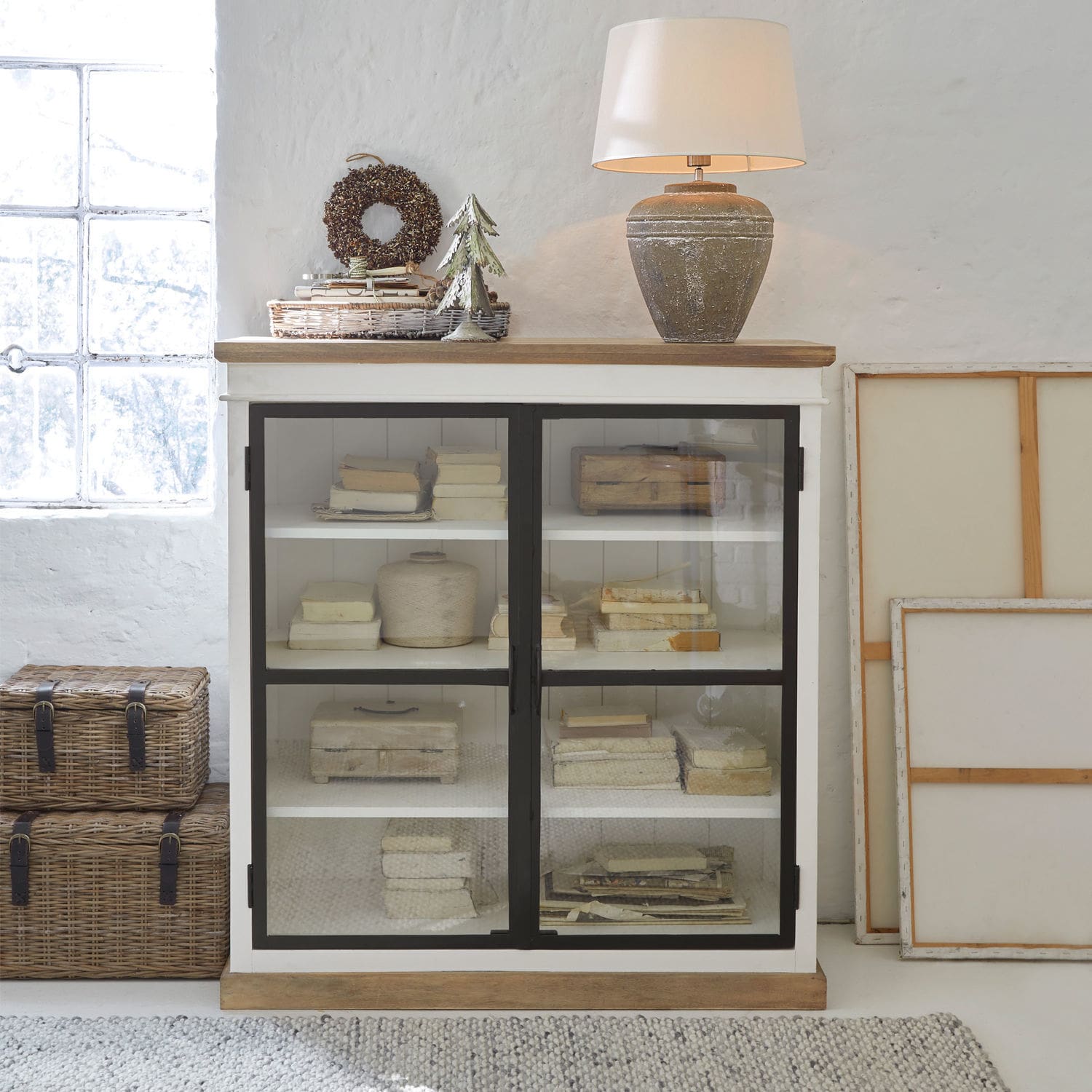 Weiße Holzvitrine mit Glastüren und Keramiklampe im Vintage-Stil auf der Ablage
