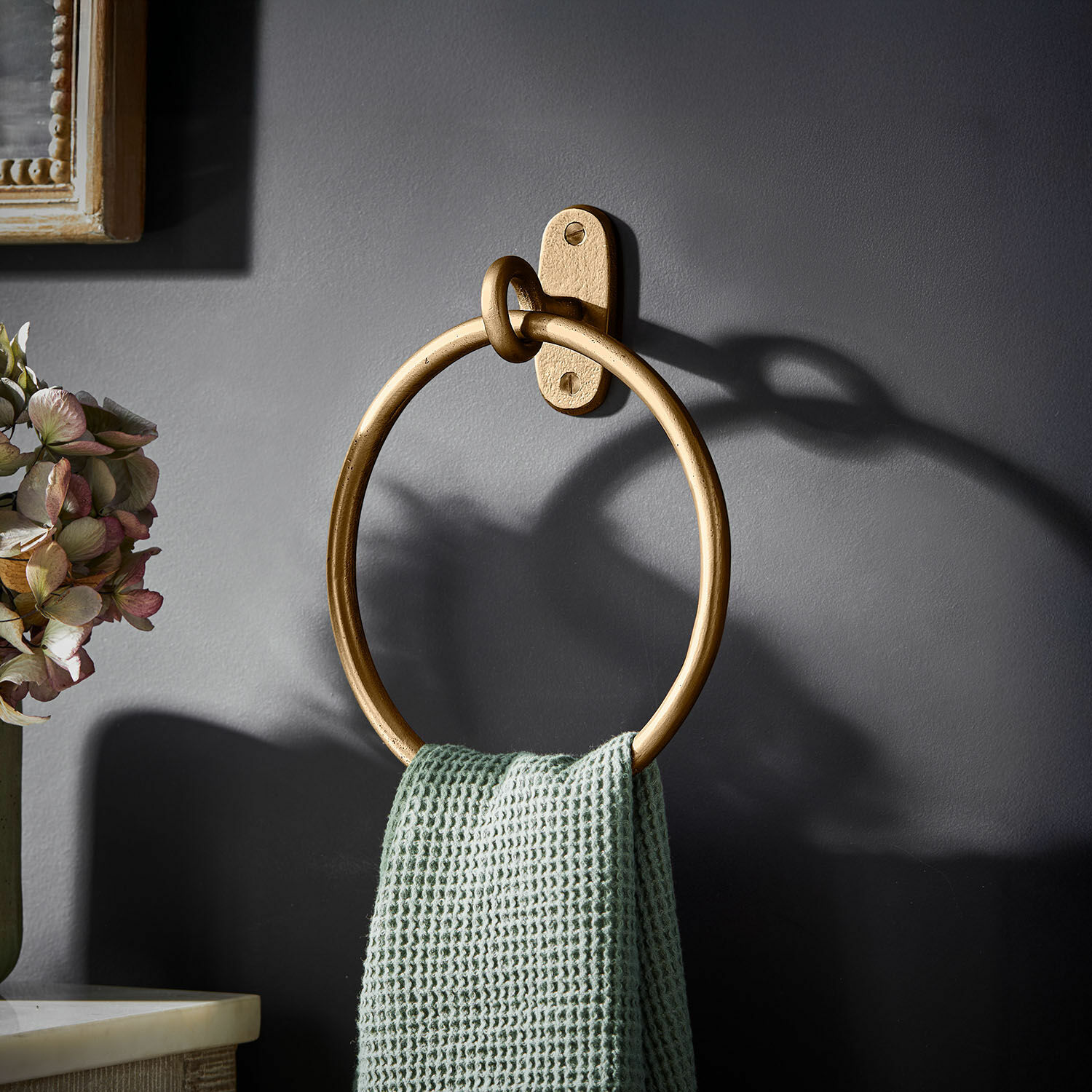 Handtuchhalter Harrowgate Goldener Metall-Handtuchhalter in Ringform an dunkelgrauer Wand mit grünem Handtuch.