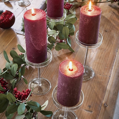 Rote Kerzen auf transparenten Glaskerzenhaltern auf Holztisch mit grünen Blättern und roten Beeren