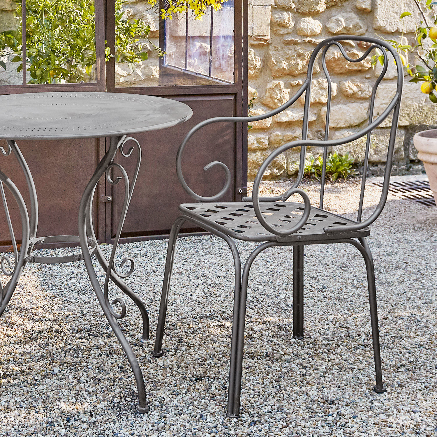Grauer Metall-Gartenstuhl mit dekorativen Armlehnen auf Kieselstein-Terrasse