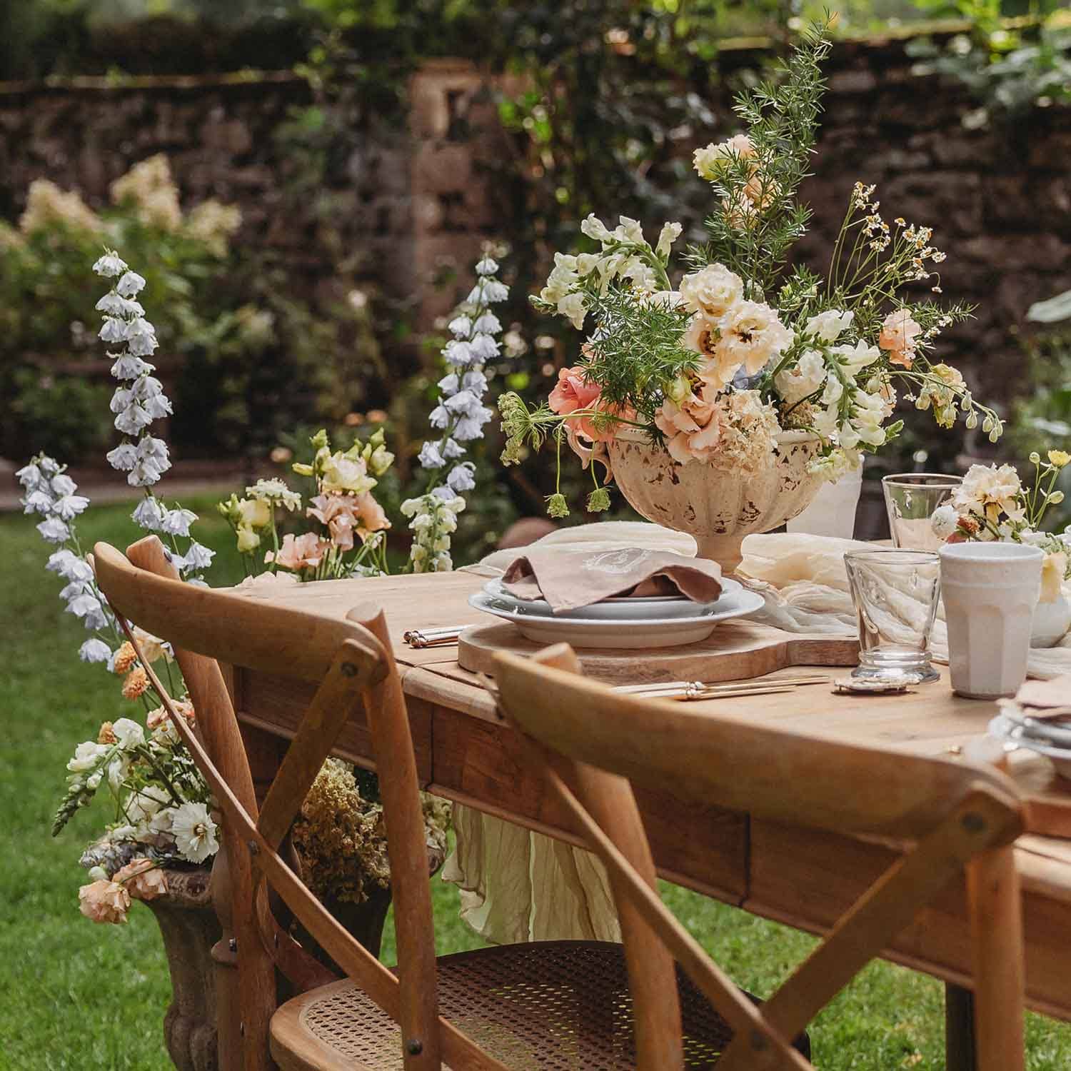 Holztisch im Garten mit rustikalen Stühlen und pastellfarbener Blumendekoration