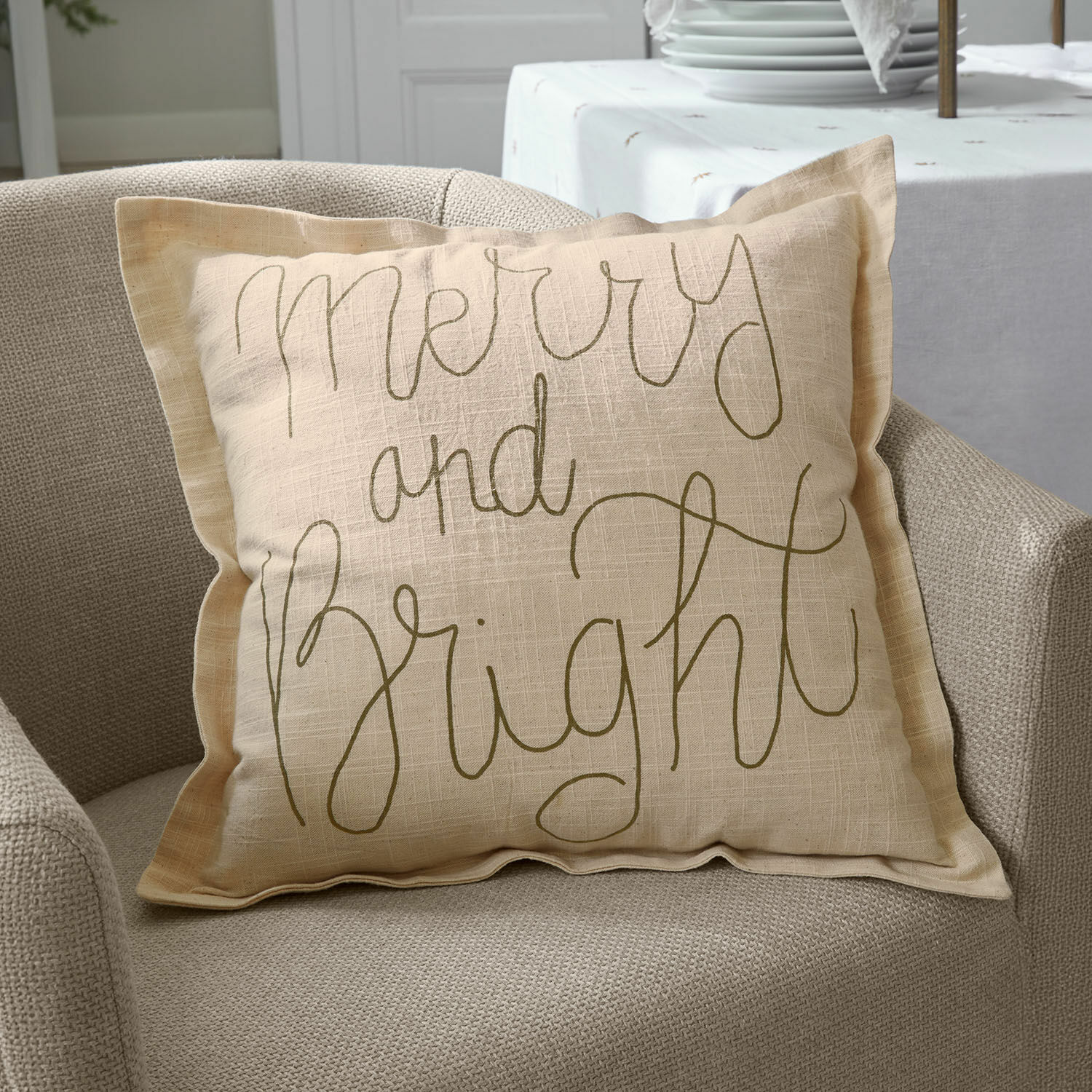 Kissenhülle Torvenna Beiges Leinen-Dekokissen mit Schriftzug Merry and Bright auf beigem Sessel, Wohnaccessoire