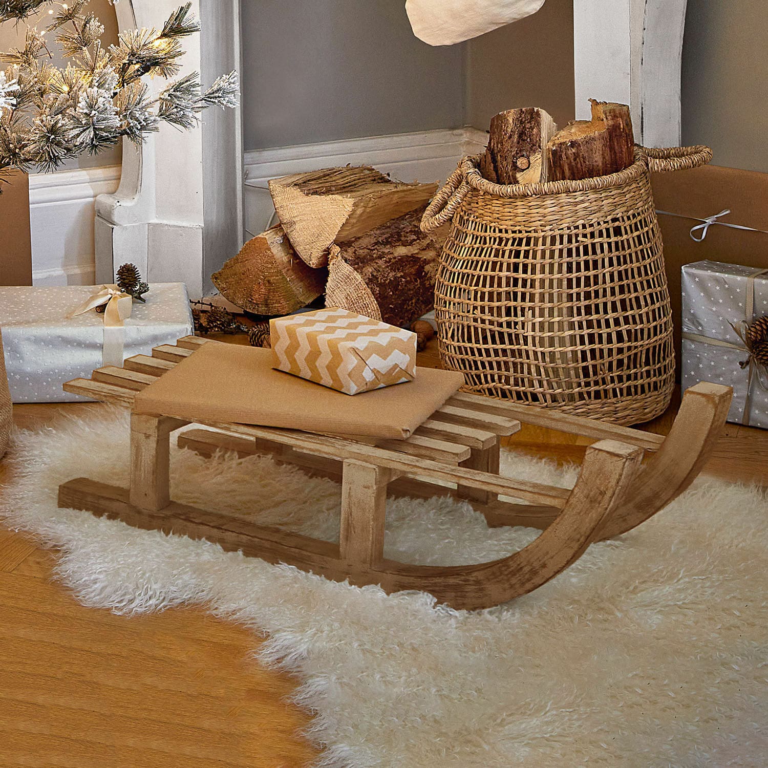 Deko-Schlitten FSC®-100% Hoekstra Dekorativer Holzschlitten auf weißem Fellteppich mit Geschenken und Korb mit Holzscheiten