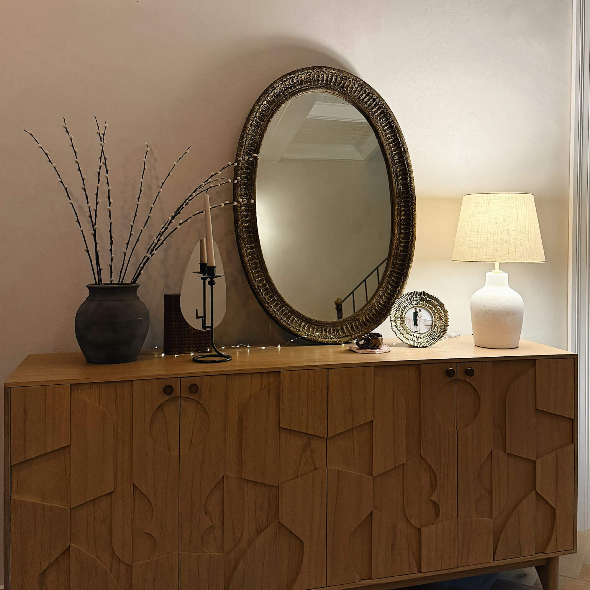 Holzkommode mit geometrischem Muster, dekoriert mit Lampe, Spiegel und Vase mit Zweigen