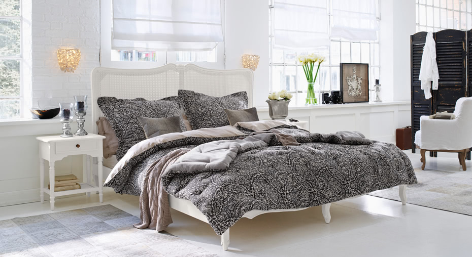 Schlafzimmer im Landhausstil mit weißem Bett und schwarz-grau gemusterter Bettwäsche