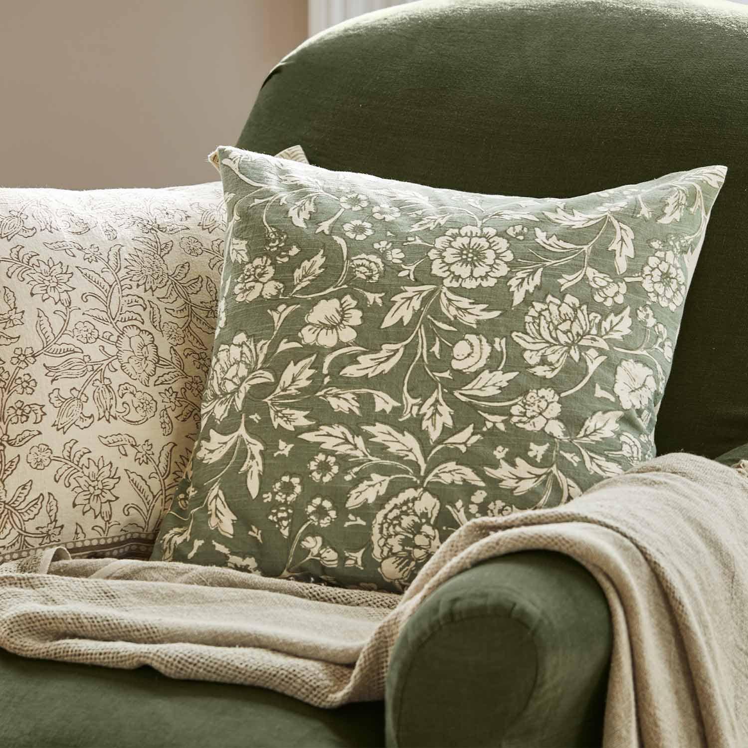 Grünes Dekokissen mit weißem Blumenmuster auf grünem Sessel mit beiger Decke im Wohnzimmer