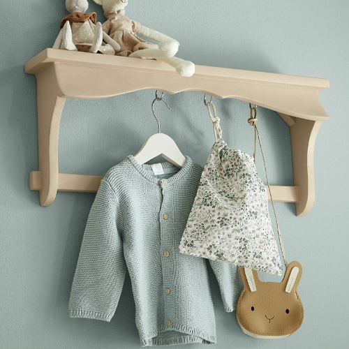 Beige Holz-Wandregal mit Haken, an dem ein hellblauer Pullover und ein Blumenmuster-Beutel hängen
