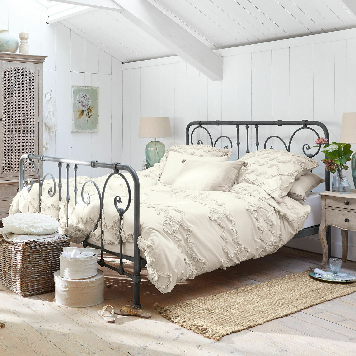 Vintage Metallbett mit cremefarbener Bettwäsche und dekorativen Kissen in hellem Schlafzimmer
