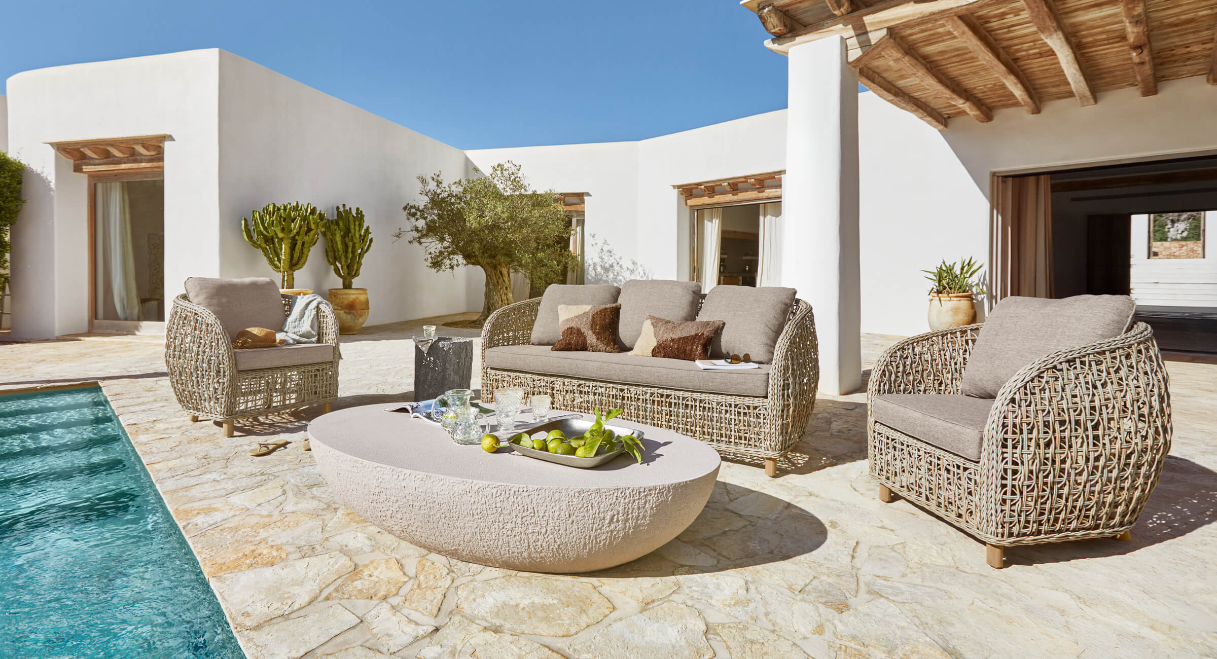 Beiges Rattan-Gartenmöbel-Set mit Polstern auf Steinterrasse neben Pool im mediterranen Stil