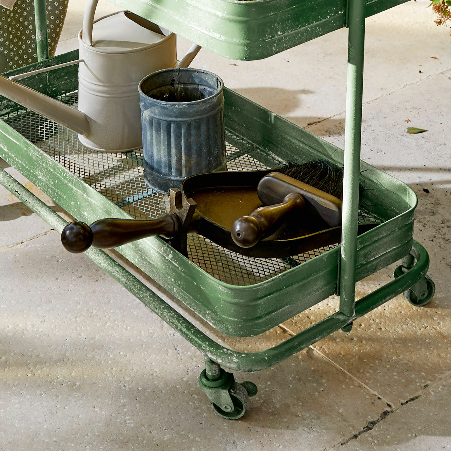 Grüner Metallwagen auf Rollen mit Gartengeräten und Gießkanne für Gartenarbeit