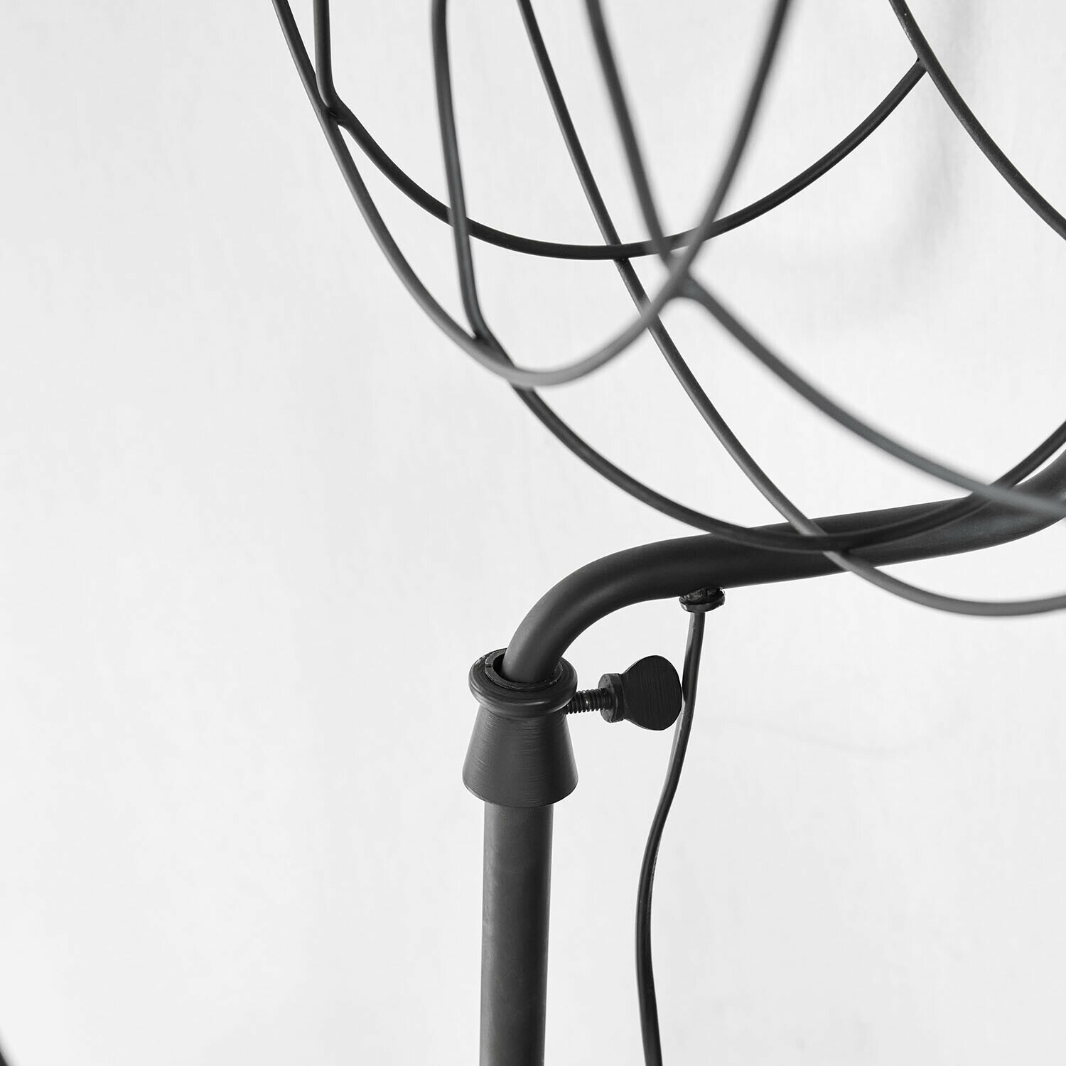 Schwarze Metallstruktur einer Lampe mit verstellbarem Arm und Stromkabel vor weißem Hintergrund