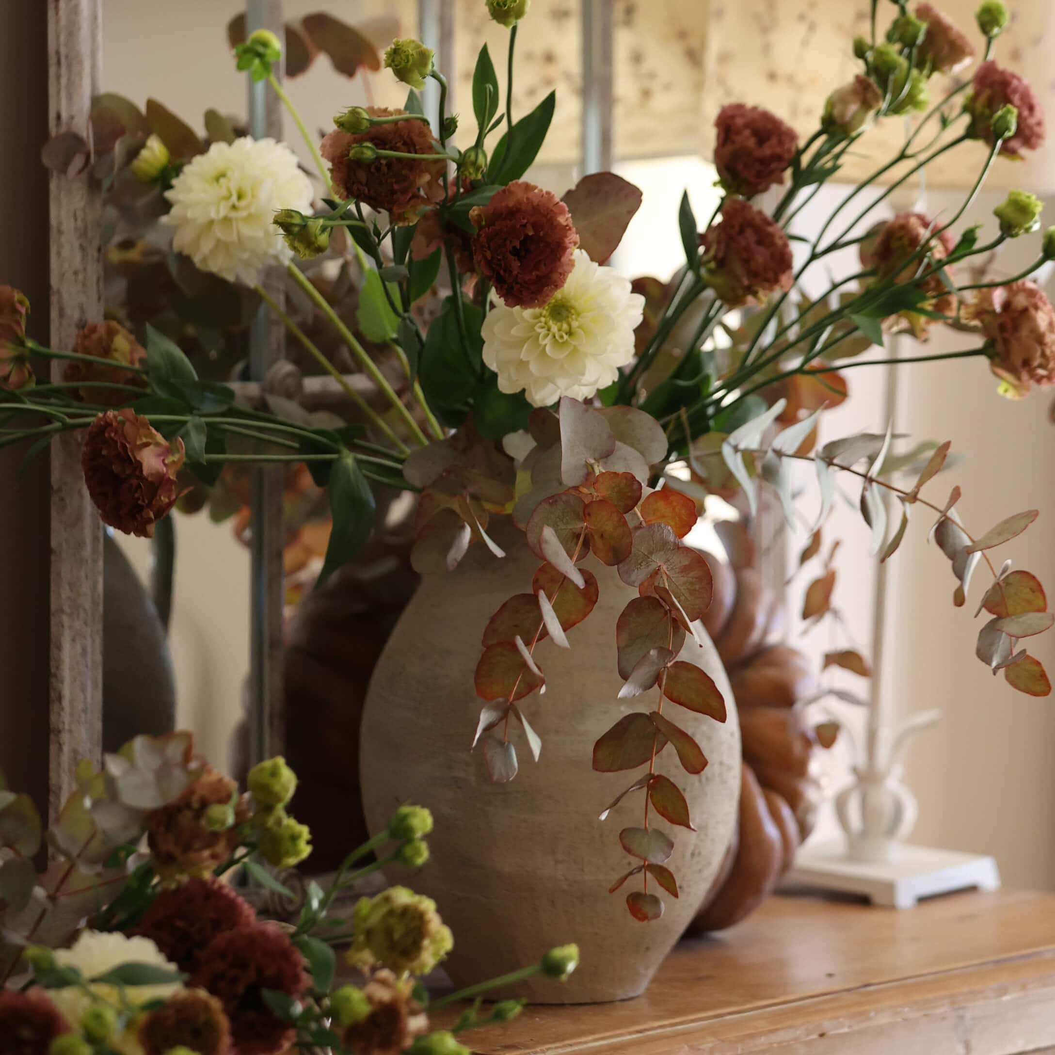 Beige Keramikvase mit weiß-braunem Blumenstrauß auf dekorativem Holztisch