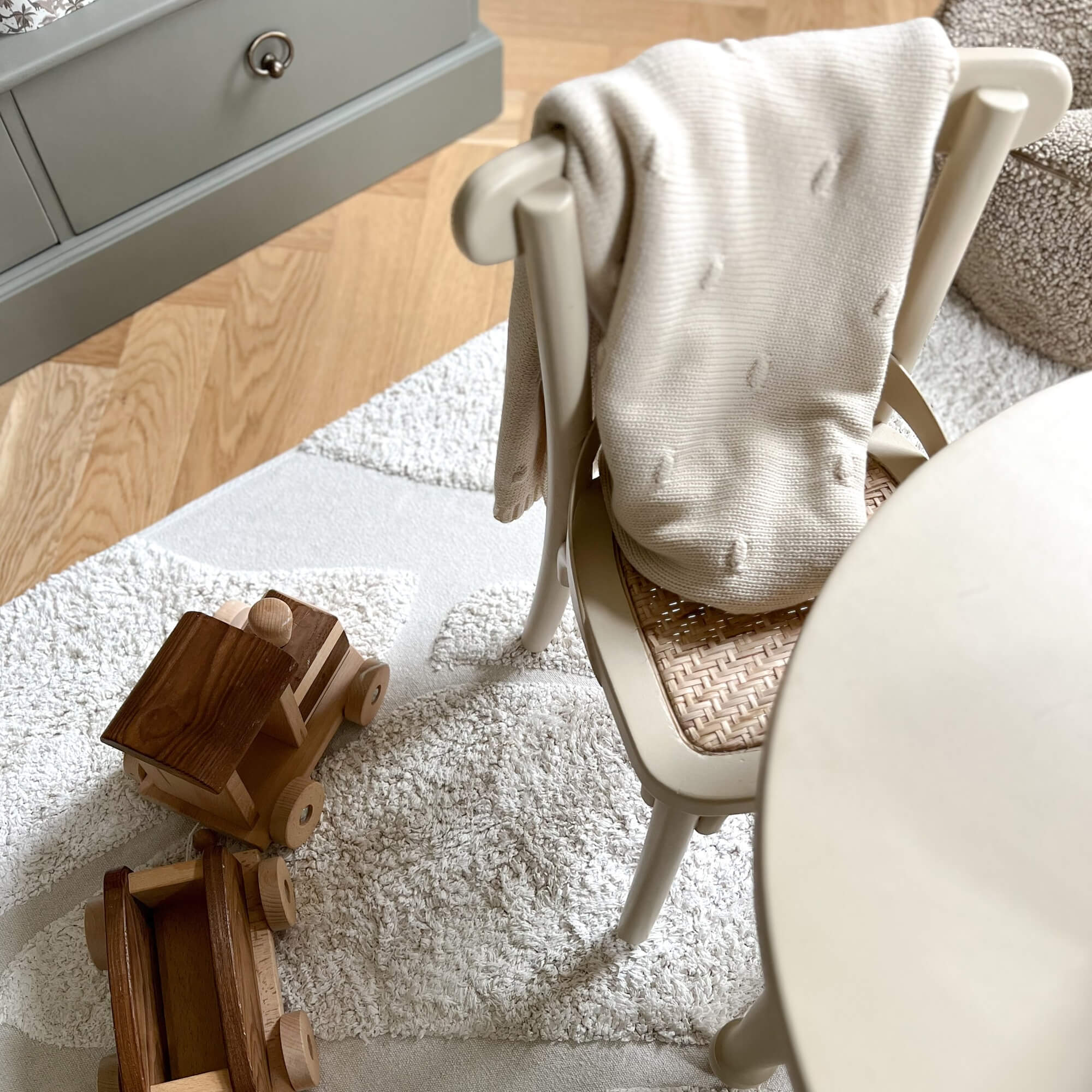 Beige gestrickte Decke auf Stuhl mit geflochtenem Sitz neben Holzspielzeug auf hellem Teppich