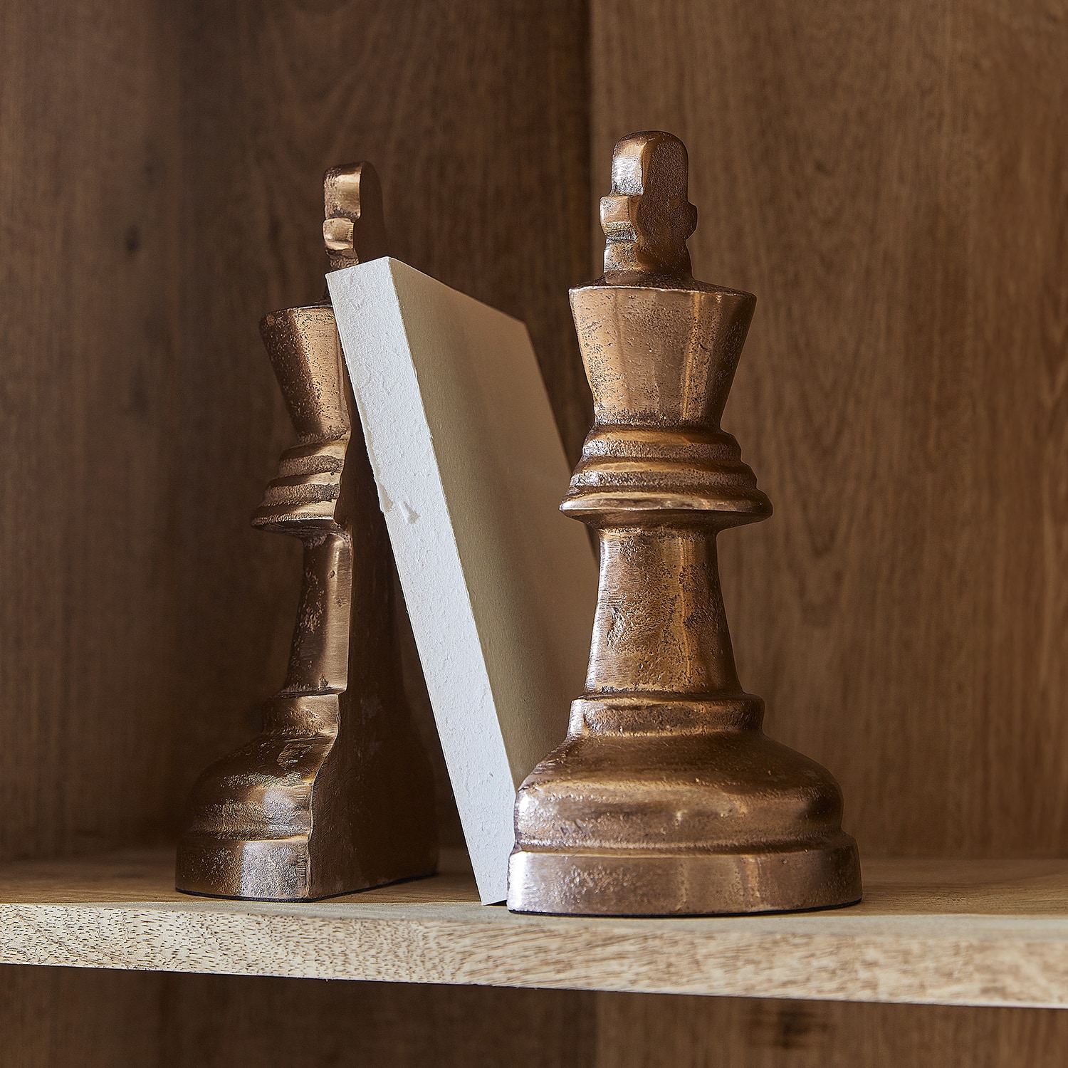 Buchstützen in Schachfigurenform aus kupferfarbenem Material auf Holzregal
